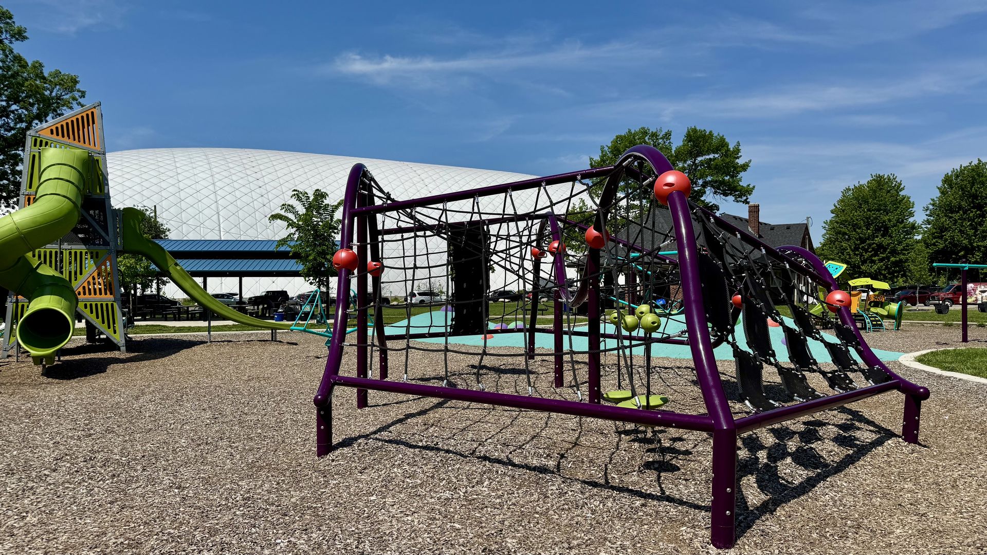 Playground equipment on woodchips. A climbing structure and a slide in the background