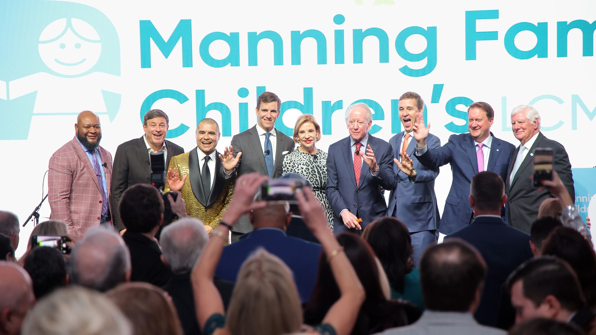 Nine people gather together onstage and smile for photos. Behind them is a logo that says Manning Family Children's LCMC.