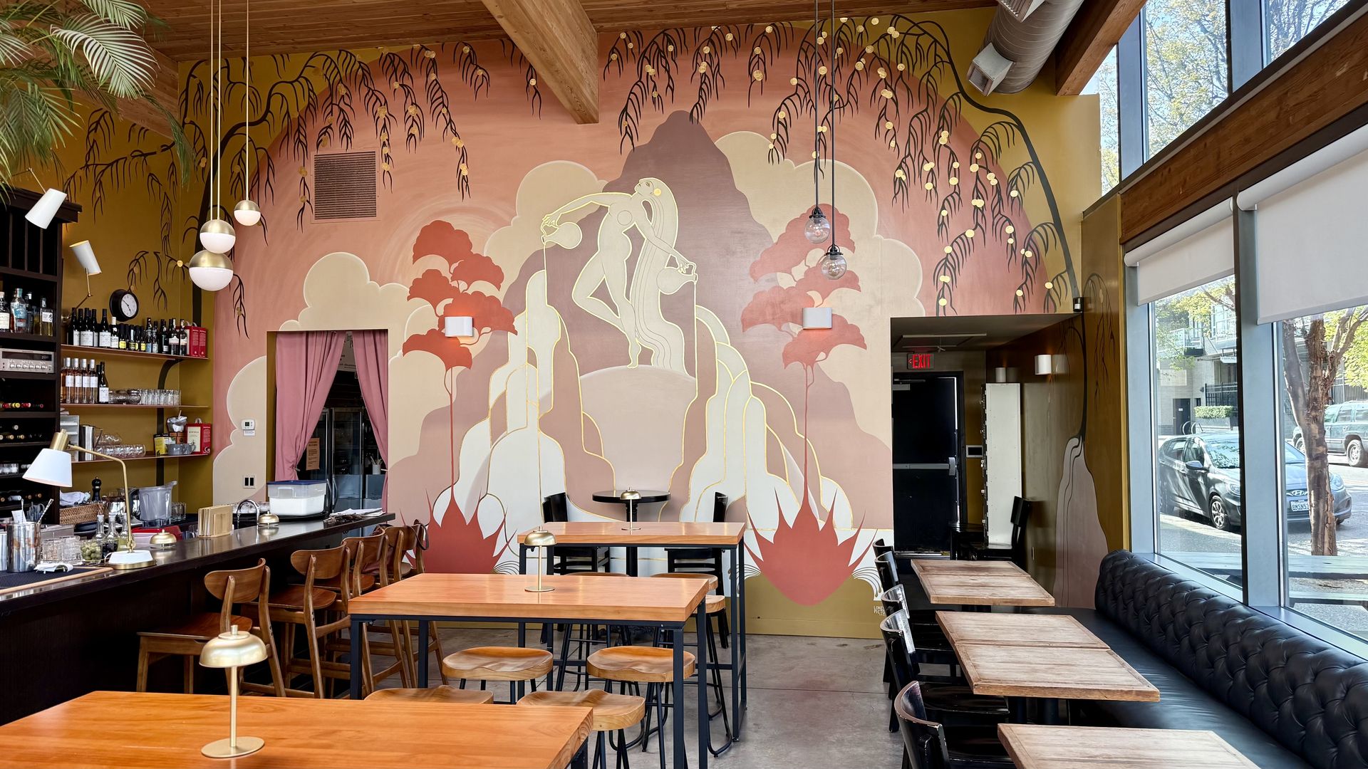 A photo of the inside of a restaurant with a pink and purple mural on the backside wall depicting a figure on the top of a mountain.