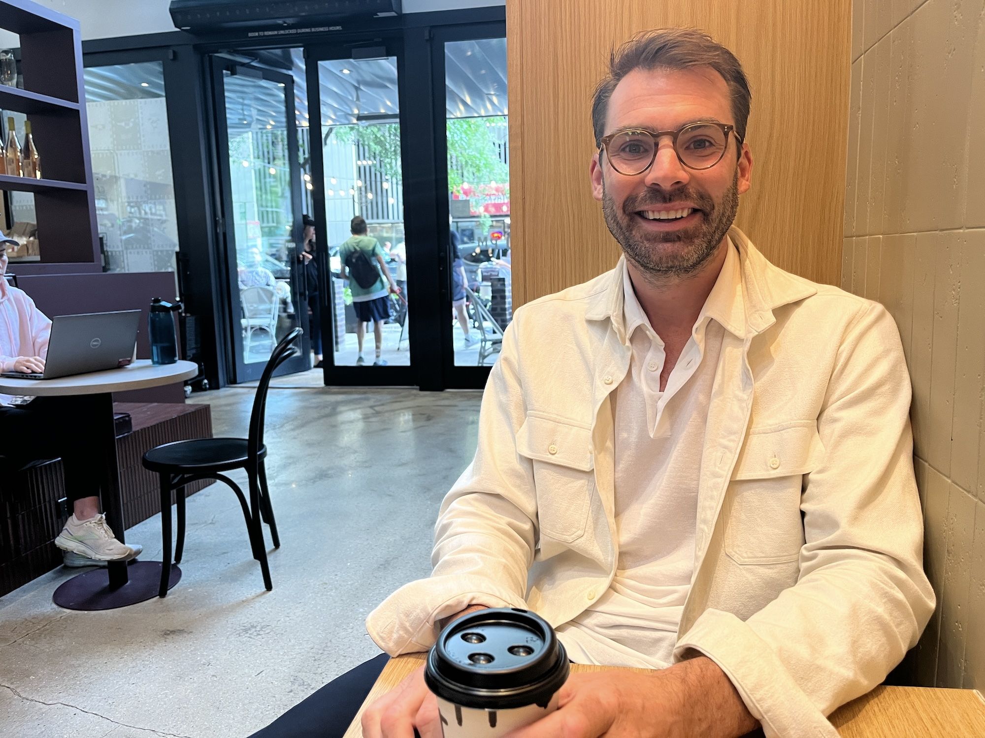 Man in white shirt jacket wearing glasses sitting in a booth at a restaurant.