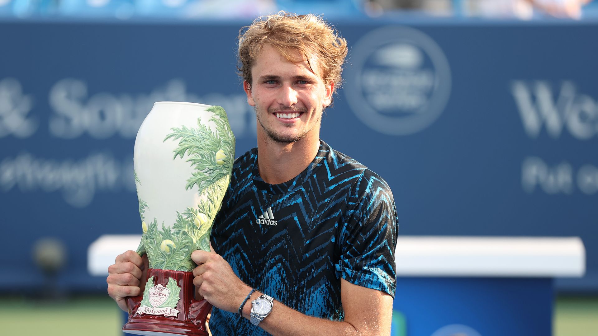Alexander Zverev of Germany holds a Rookwood Pottery-inspired vase trophy after winning Western & Southern Open (now the Cincinnati Open) in 2021. He's smiling at the camera, posing and wearing a blue tennis shirt by Adidas. (Photo by Matthew Stockman/Getty Images)