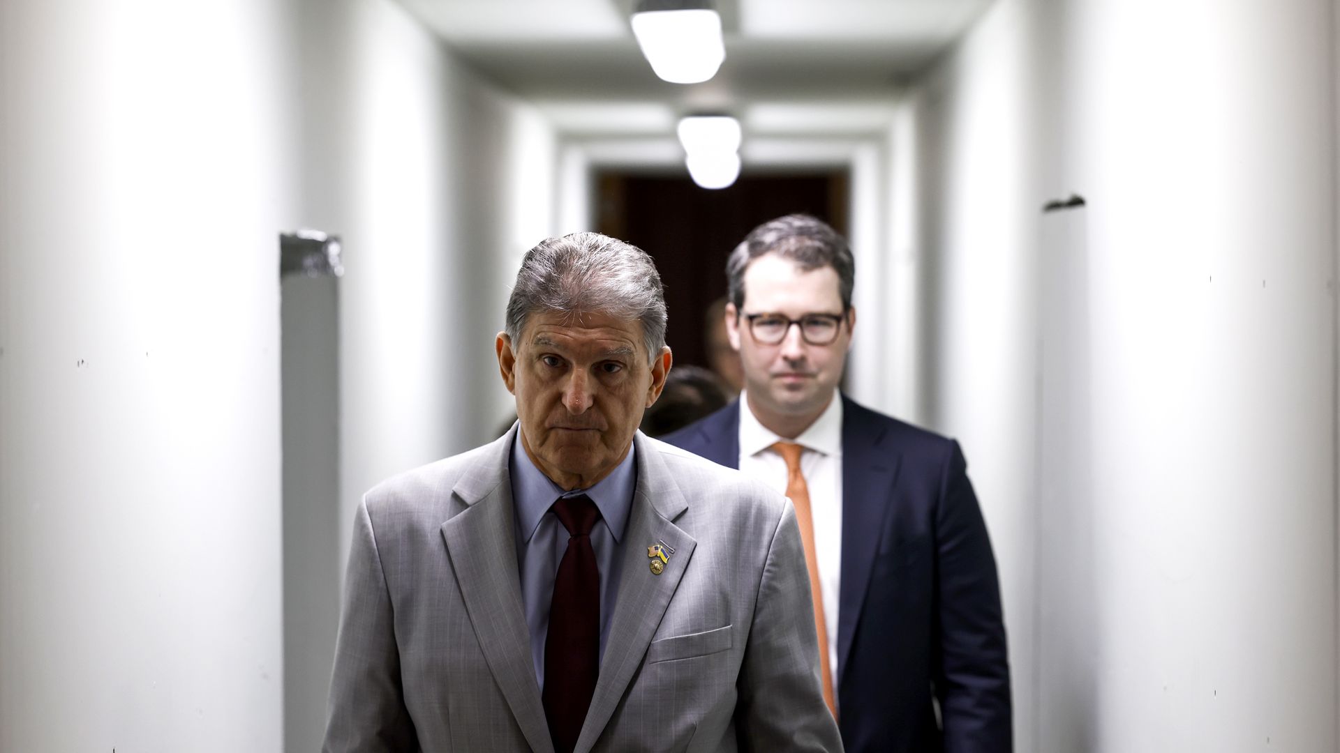Two men in suits walk purposefully down a white corridor 