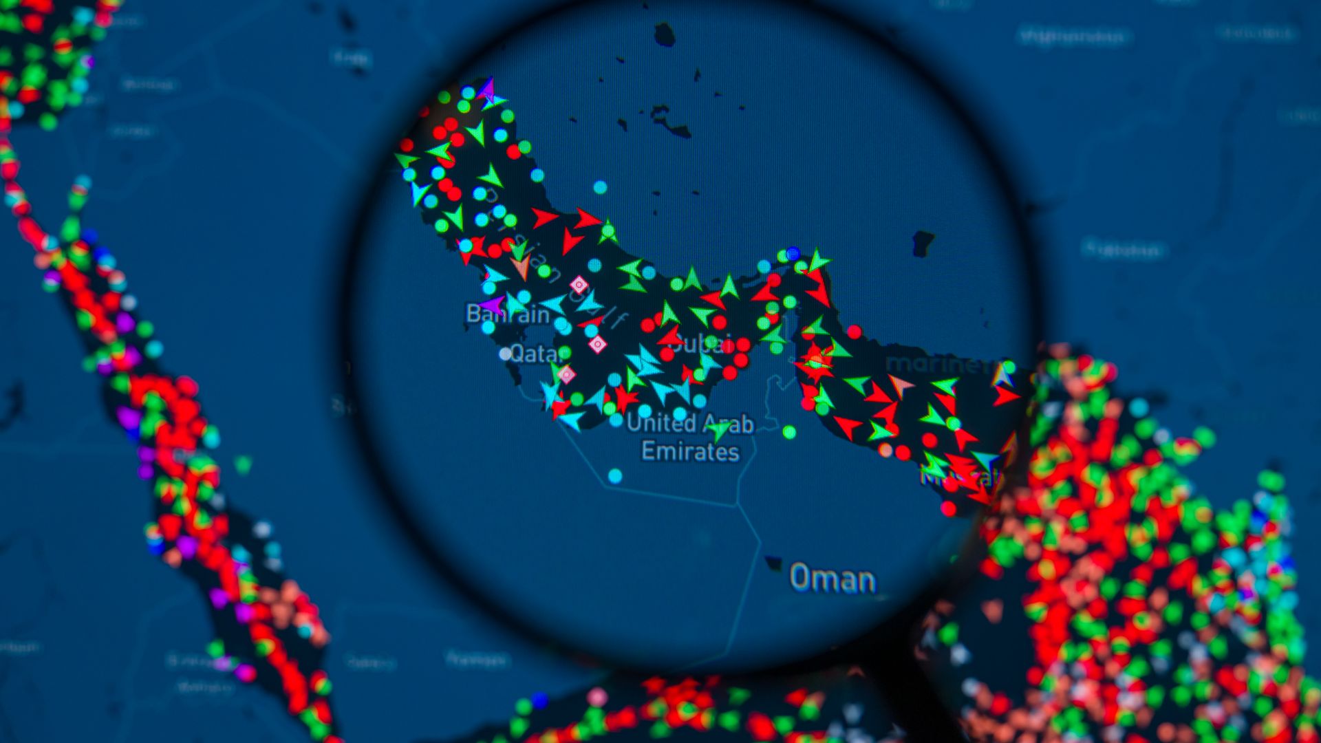 A magnifying glass highlights a digital map of ship traffic in the Strait of Hormuz, illustrating reduced vessel movements during regional tensions.