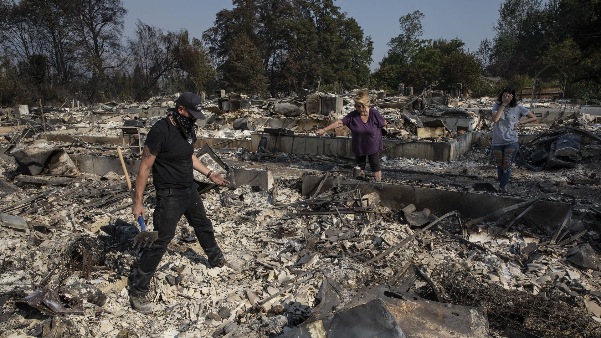 A man stands in the rubble while wearing a bandana, as two women look on from a distance