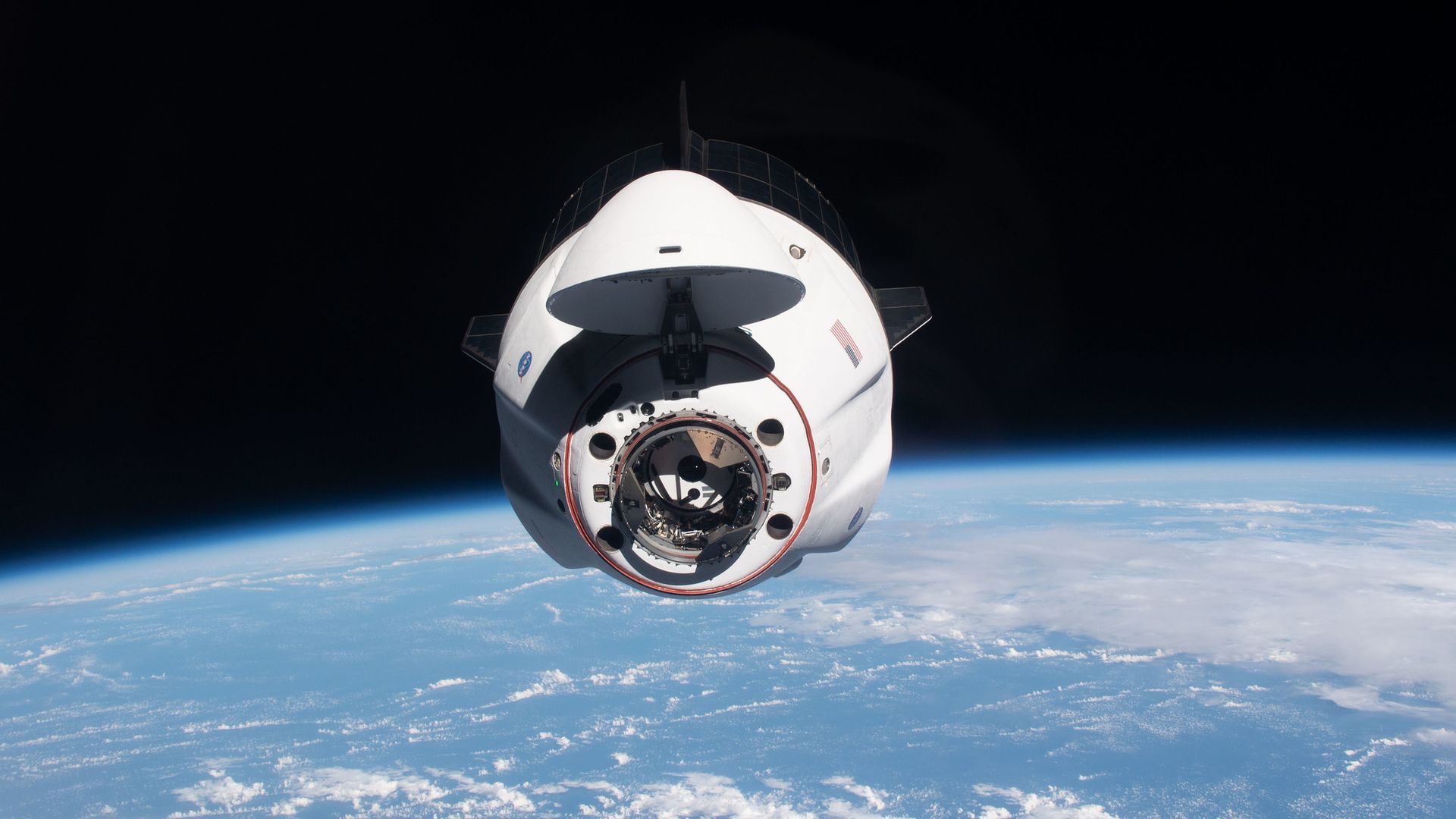 A Crew Dragon coming in for a docking at the International Space Station while flying high above the blue Earth below