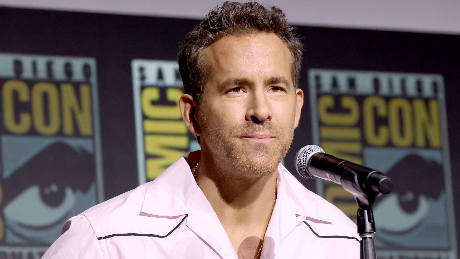 photo of Ryan Reynolds, a man in pink shirt talking into a mic on stage