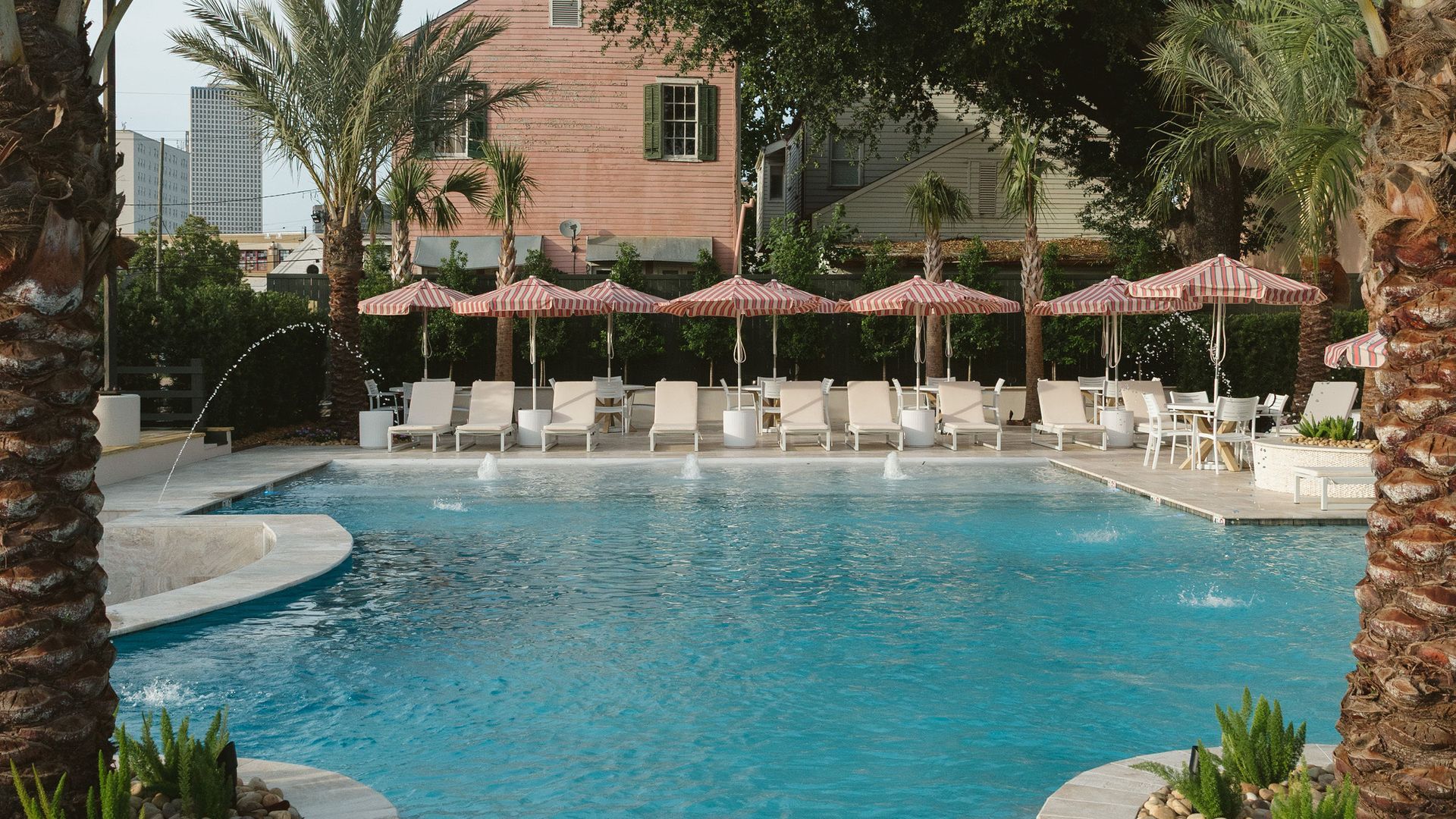 A pool and pool deck is viewed through two palm trees.