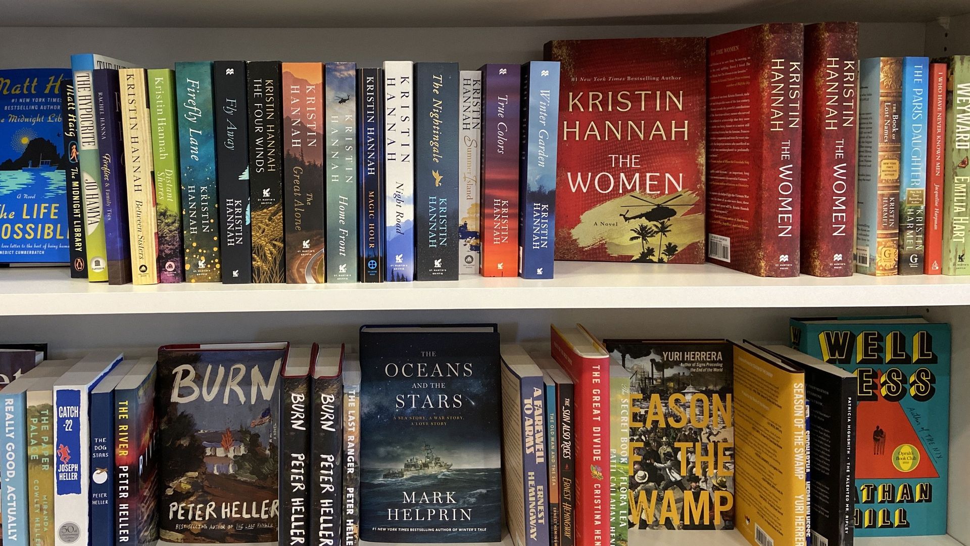 Copies of books on a shelf, including "The Women" by Kristin Hannah.