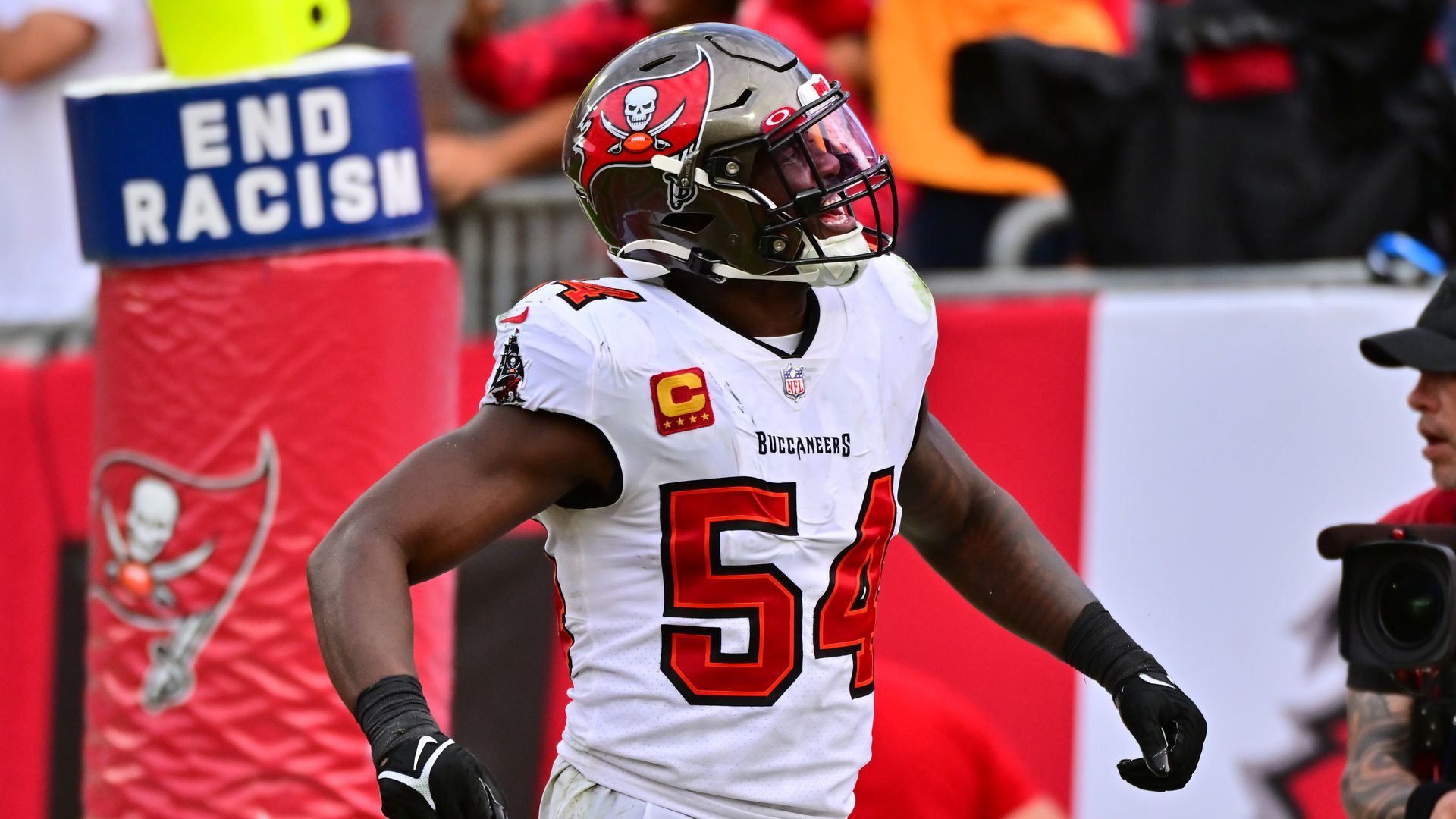 Lavonte David #54 of the Tampa Bay Buccaneers yells on the field with a sign that says "End Racism" behind him.