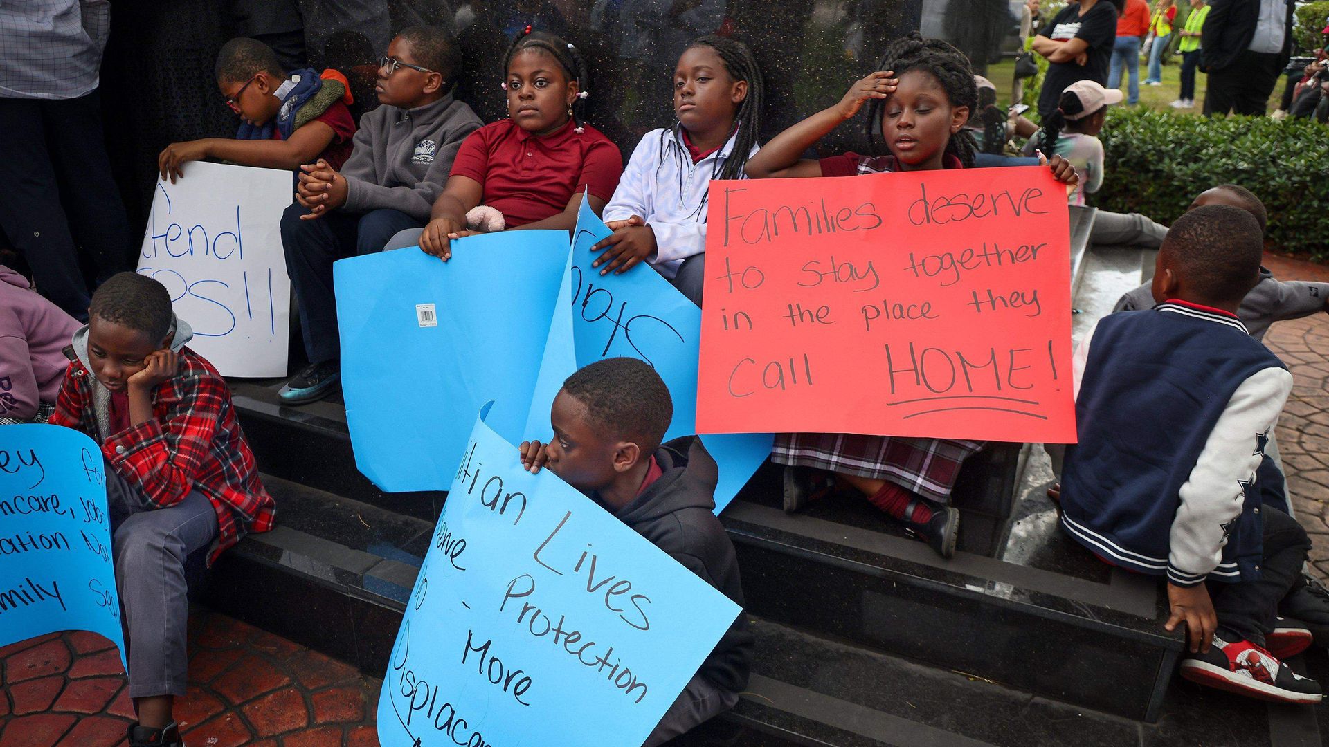 Children bearing signs in support of TPS for Haitians sit at on the steps of the Toussaint Louverture Memorial Statue in Miami on Jan. 12, 2026. (Carl Juste/Miami Herald/Tribune News Service via Getty Images)
