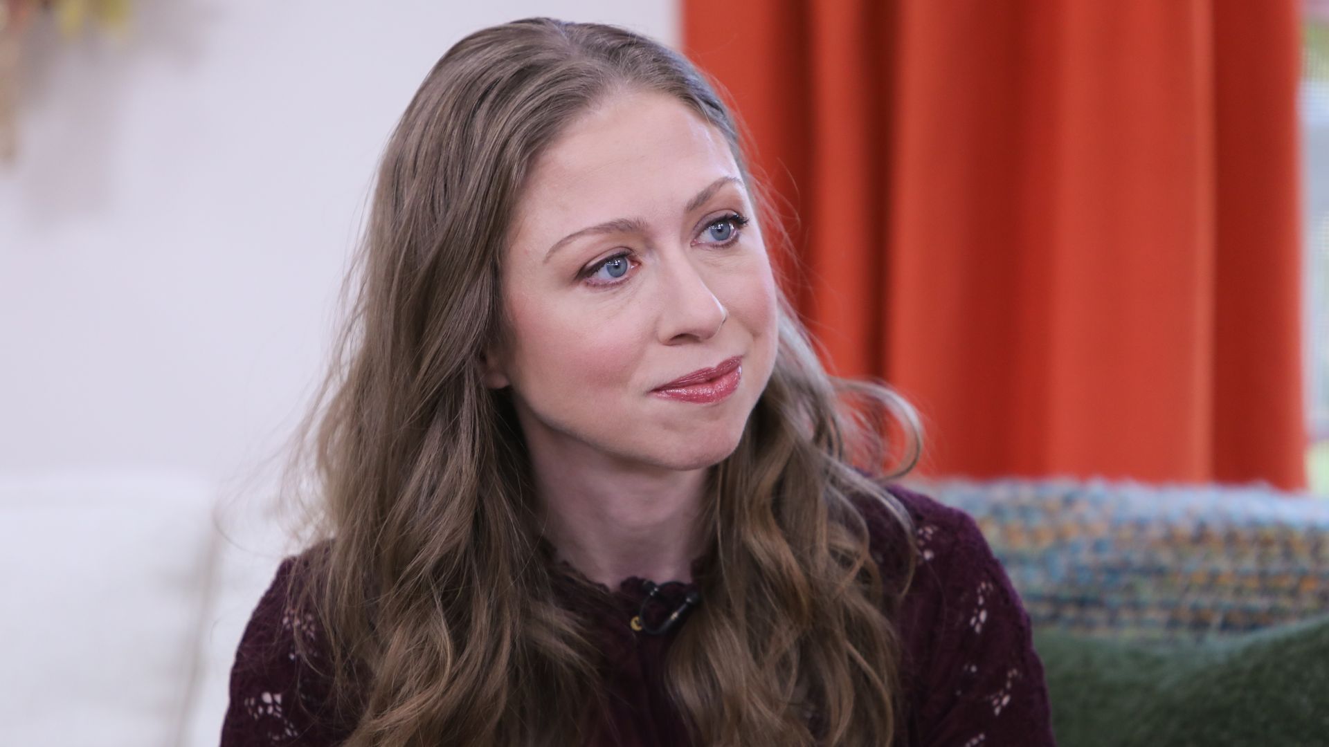 Chelsea Clinton sits and listens while wearing a red dress.