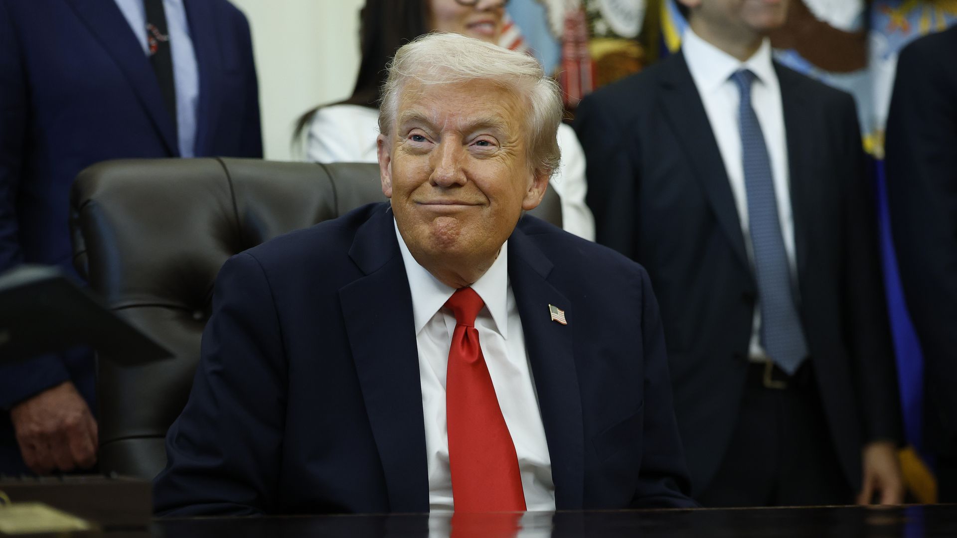 President Trump, wearing a navy jacket with a US flag pin at the top of his left lapel, white shirt and red tie