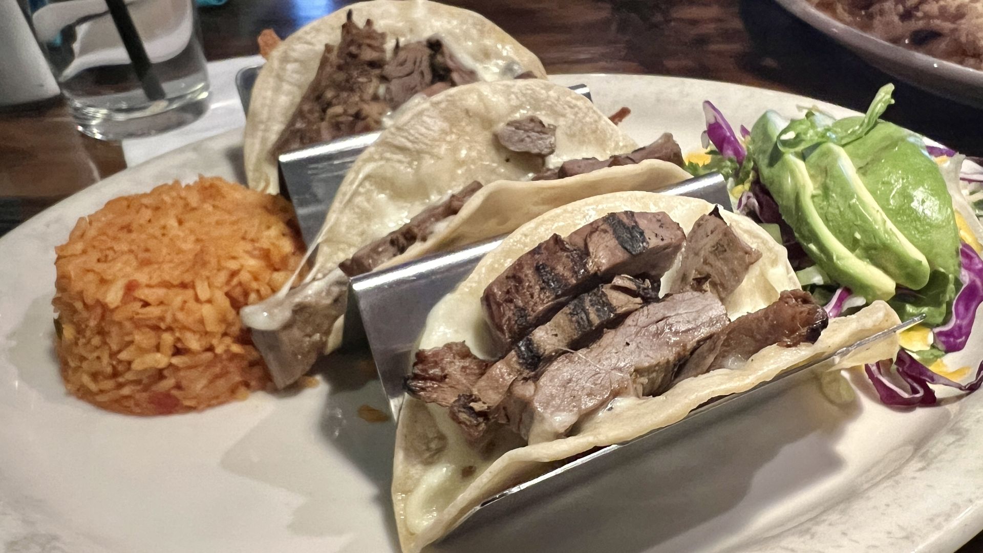 Three beef fajita tacos, with rice and avocado on the side