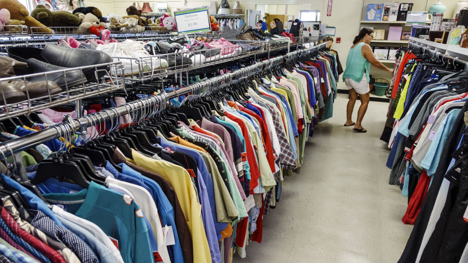 A woman scans a rack of assorted shirts. 