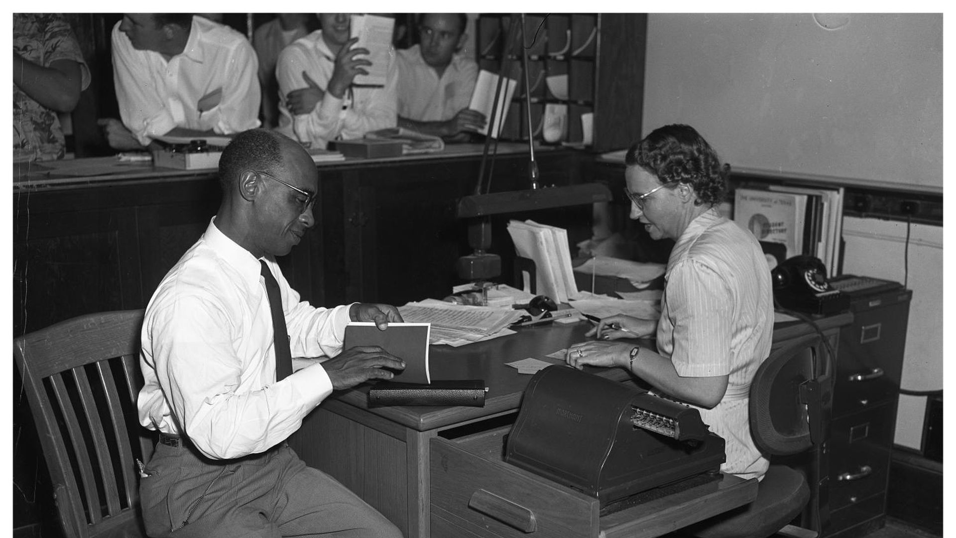 A photo of two people sitting at a desk.
