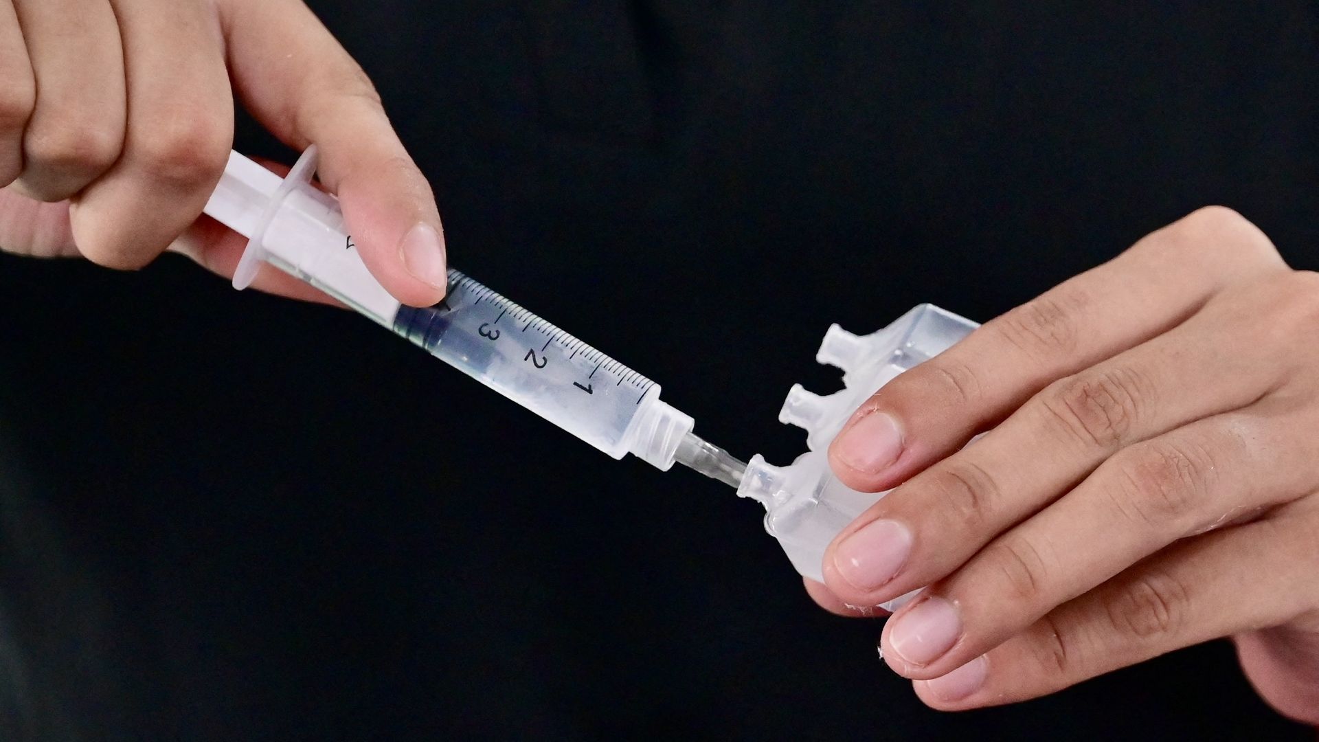 A close-up photo of a woman's hands as one plunges a syringe into a plastic container.