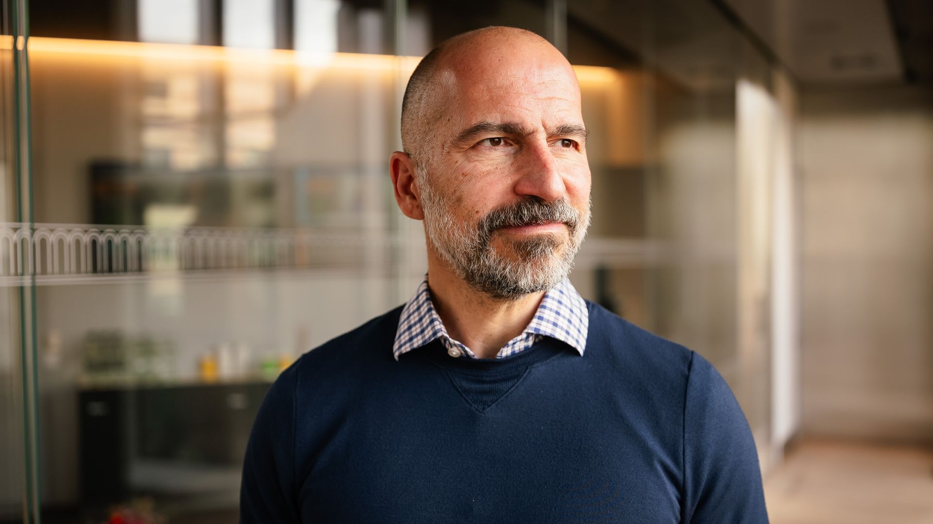 A man stands next a glass wall, looking to the right of the camera.