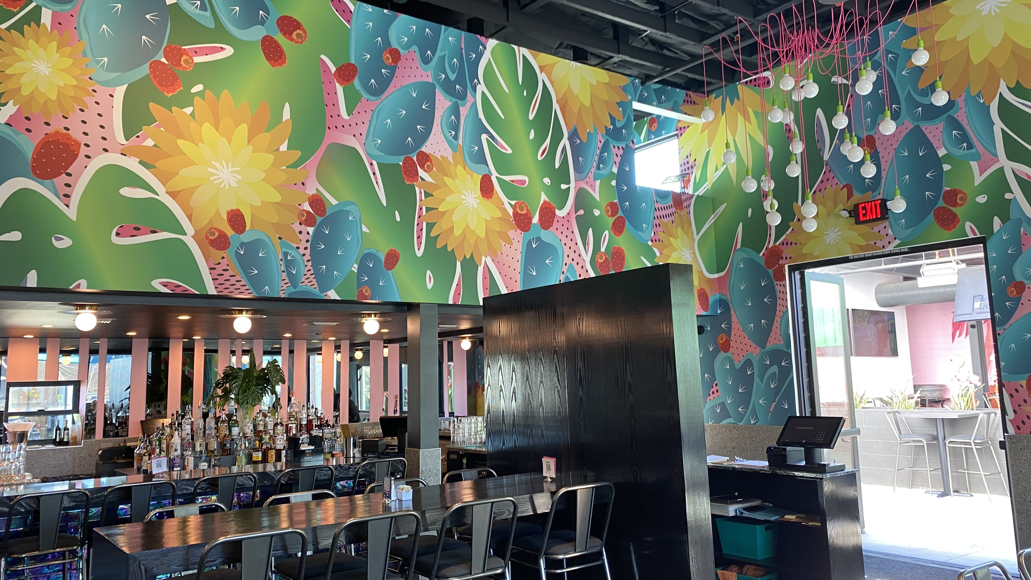 A bar with brightly colored artwork depicting leaves and prickly pear cactus above it. 