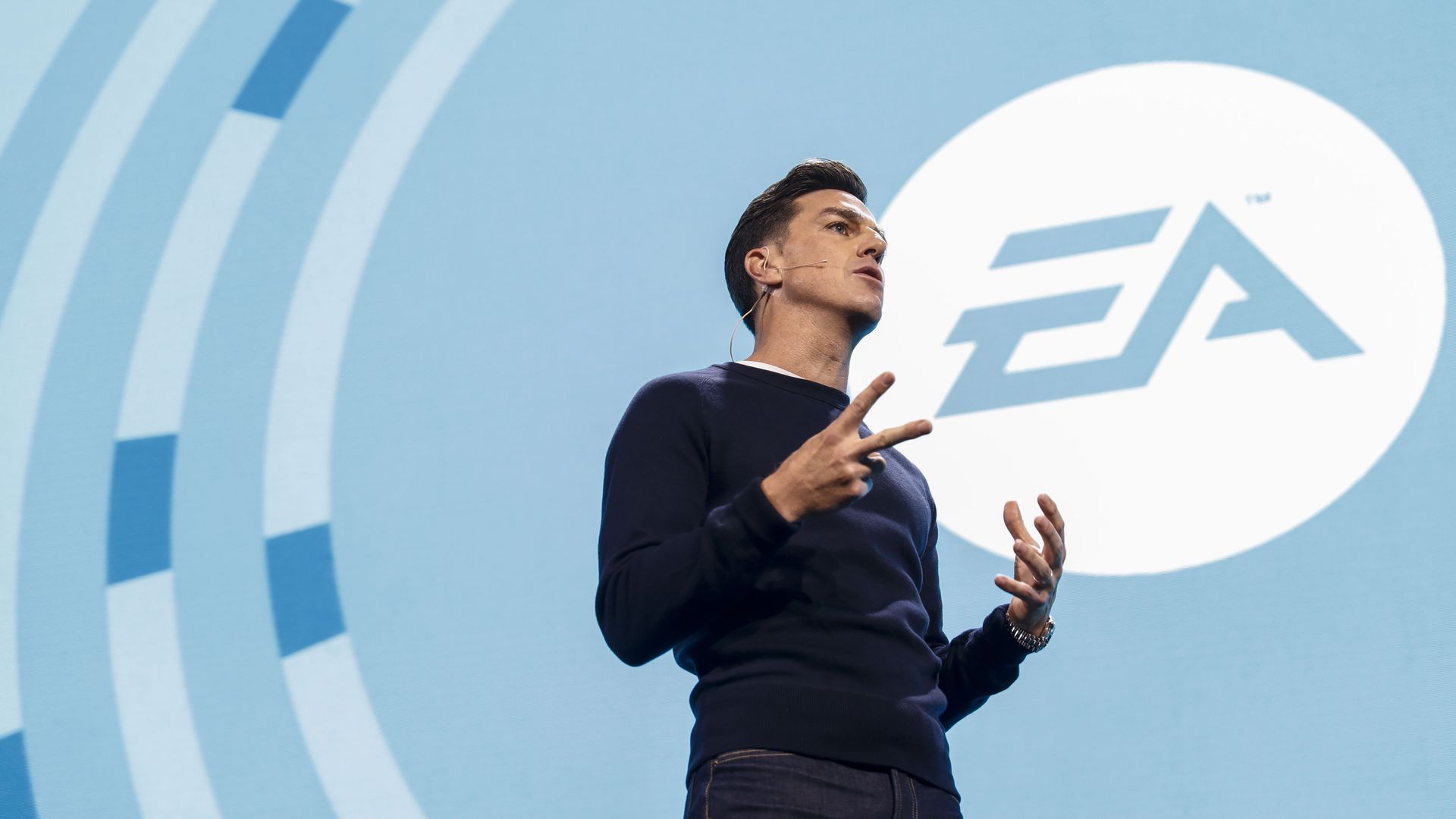 Picture of EA CEO Andrew Wilson standing on a stage in front of an EA logo