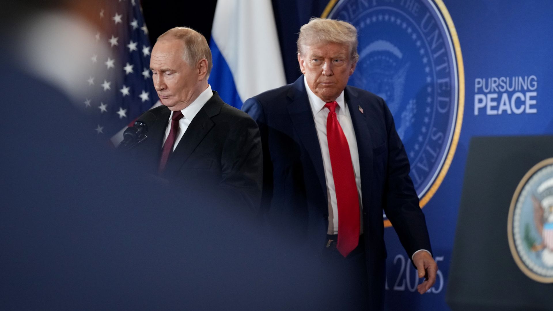 Russian President Vladimir Putin, wearing a black jacket, white shirt and purple tie, and President Trump, wearing a navy jacket with a US flag pin at the top of his left lapel, white shirt and red tie, arrive for a press conference at Joint Base Elmendorf-Richardson in Anchorage, Alaska.