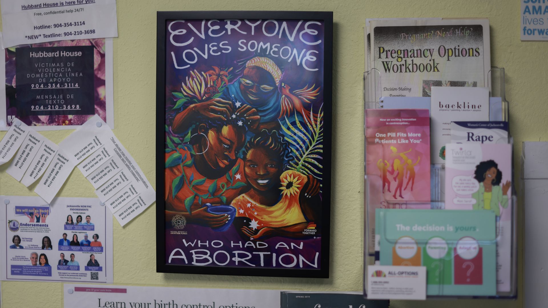 posters and pamphlets in an abortion clinic. One reads "everyone loves someone who has had an abortion with an illustration of three smiling people 