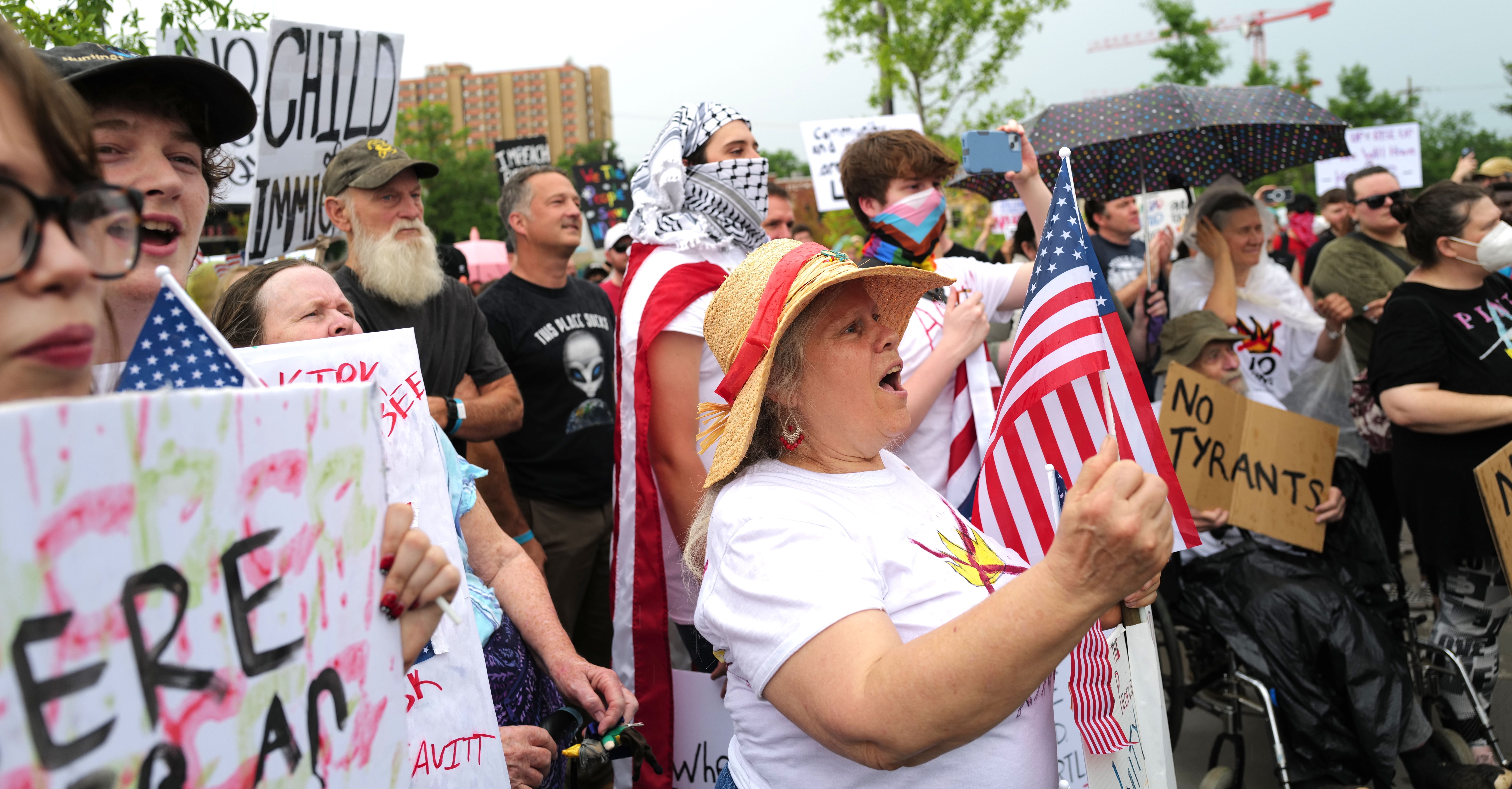 Diverse crowd of protesters holds signs and flags, chanting in the rain with messages opposing tyranny and supporting rights.