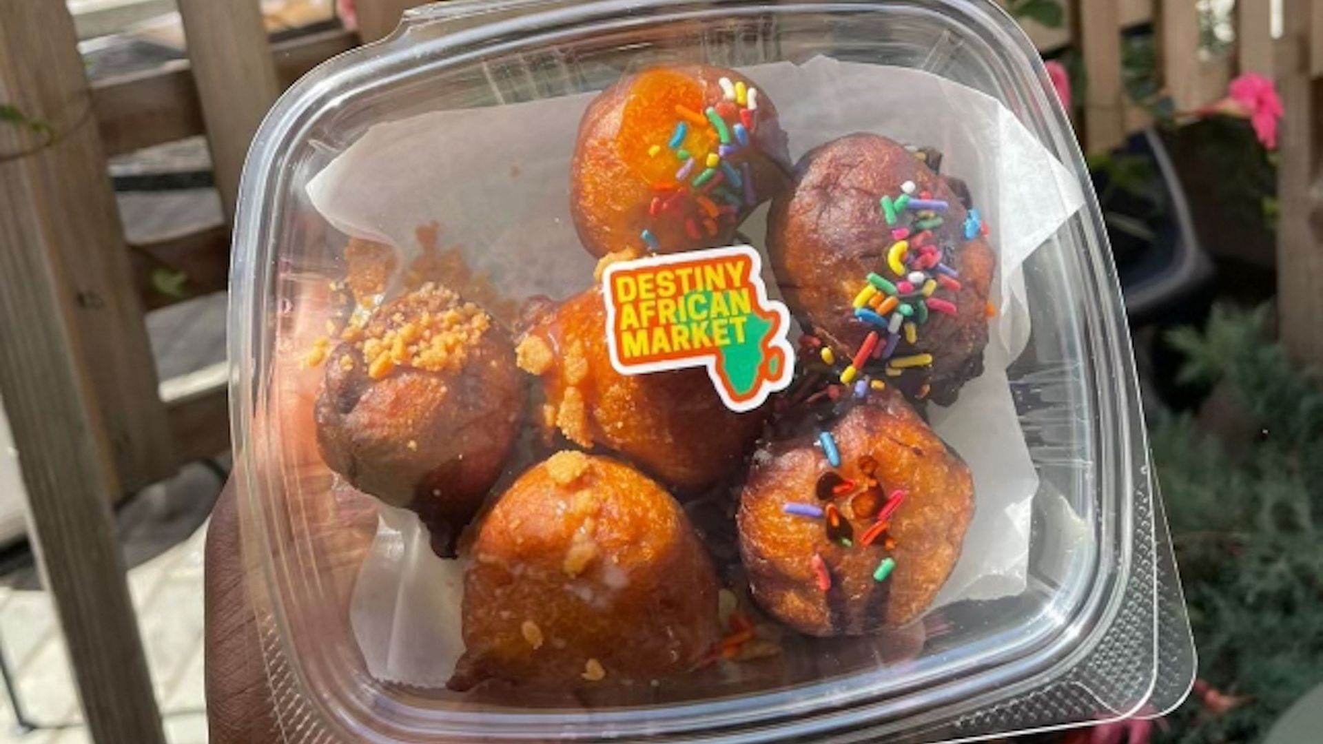 A person holds a plastic container filled with puff-puff pastries, or Nigerian fried dough balls covered in chocolate.