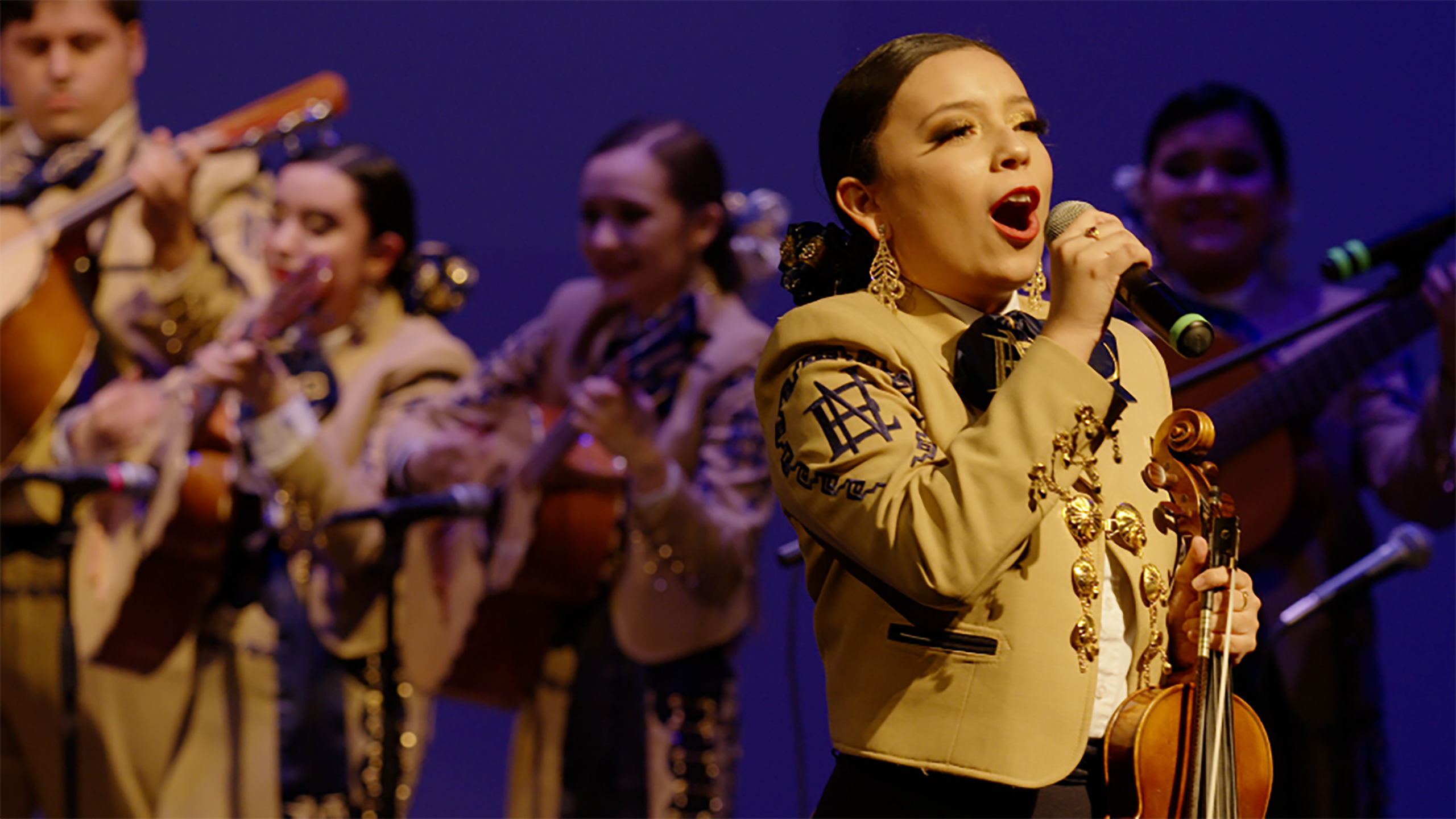 A group of teenage mariachi players performing on stage.