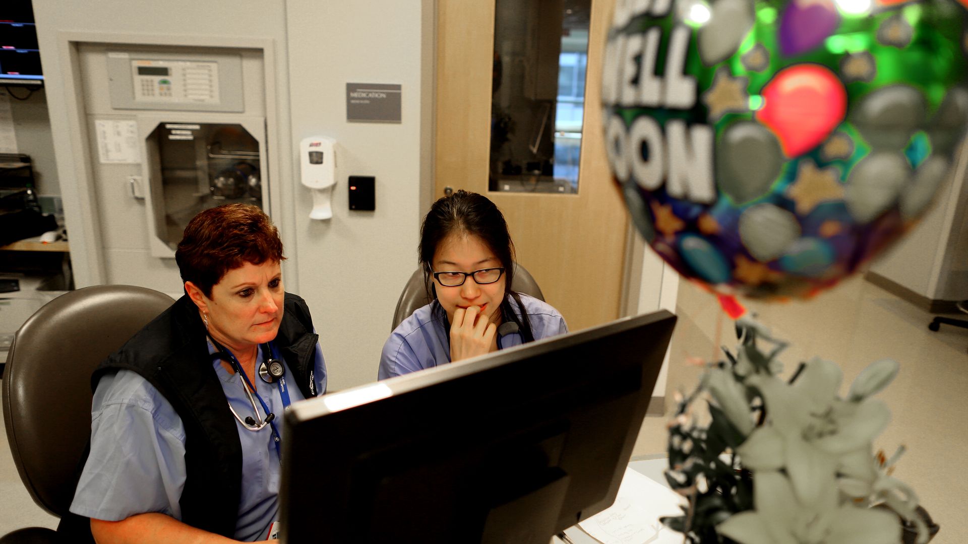 Two nurses look at a computer at a hospital.
