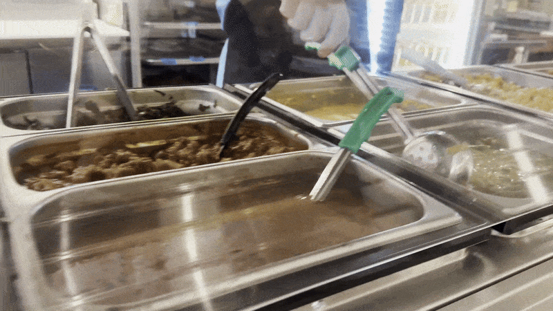 A moving image of a person shifting green beans on a cafeteria line.
