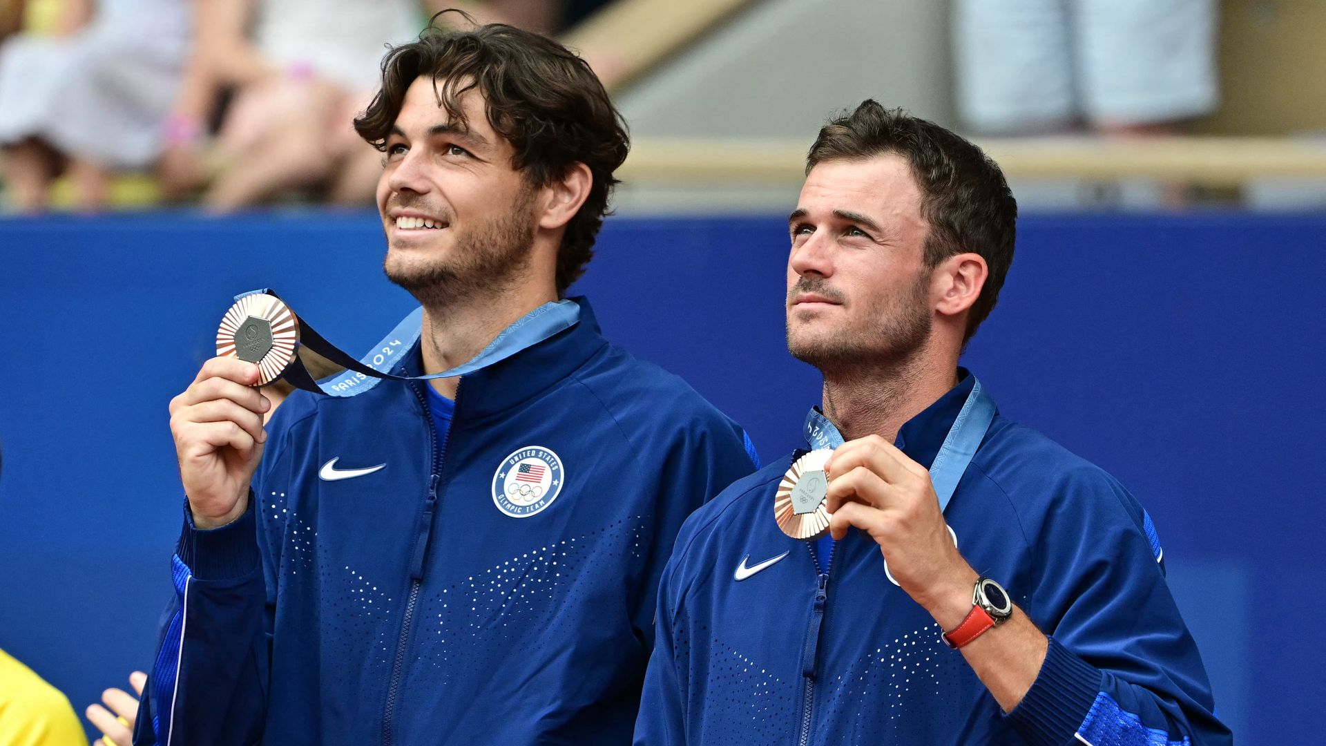 U.S. Olympic tennis players Taylor Fritz and Tommy Paul hold their bronze medals on the podium.