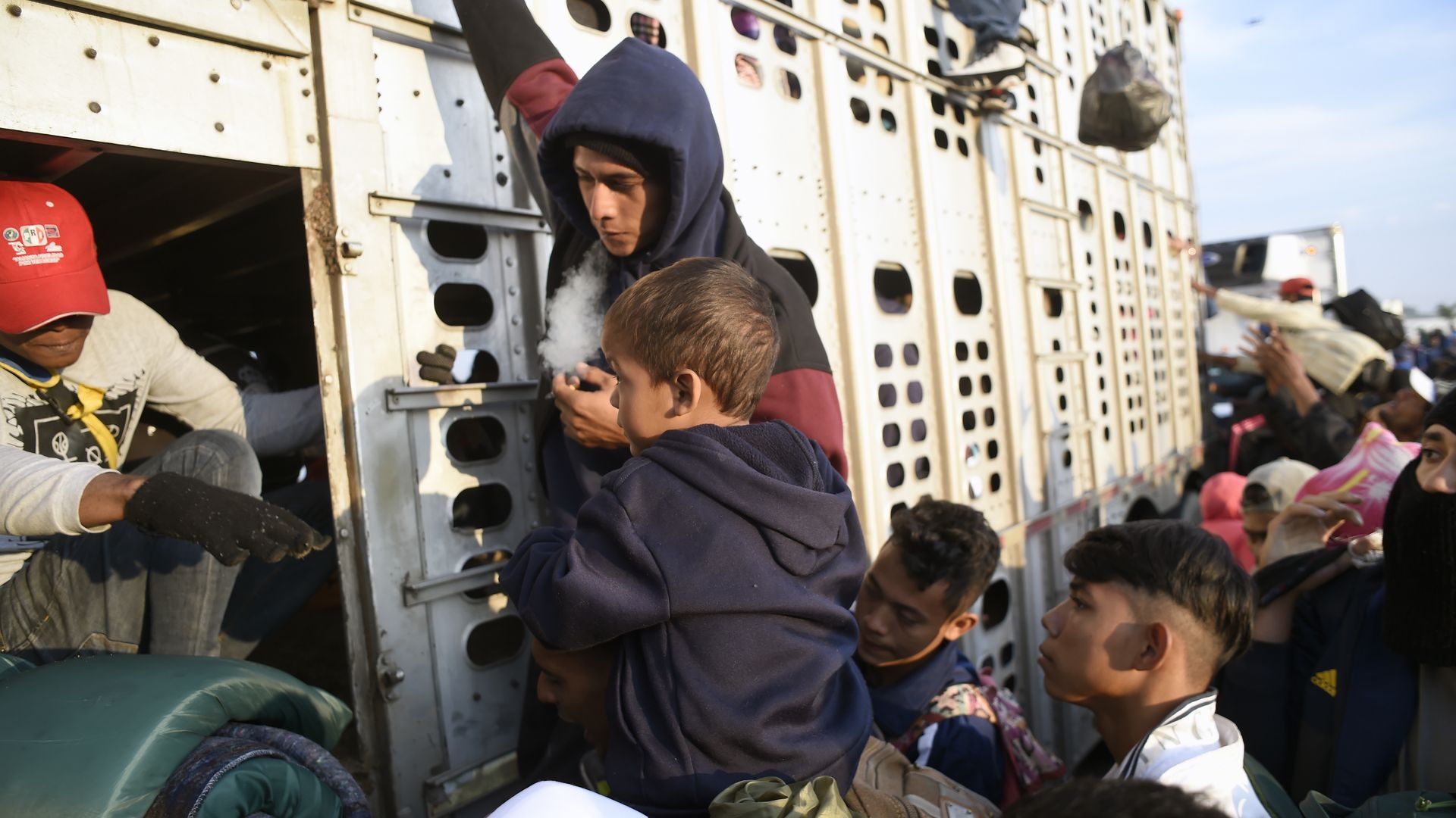 A crowd of Central American migrants, including some children, crowd around a boxcar where they are trying to get on to travel toward the U.S.