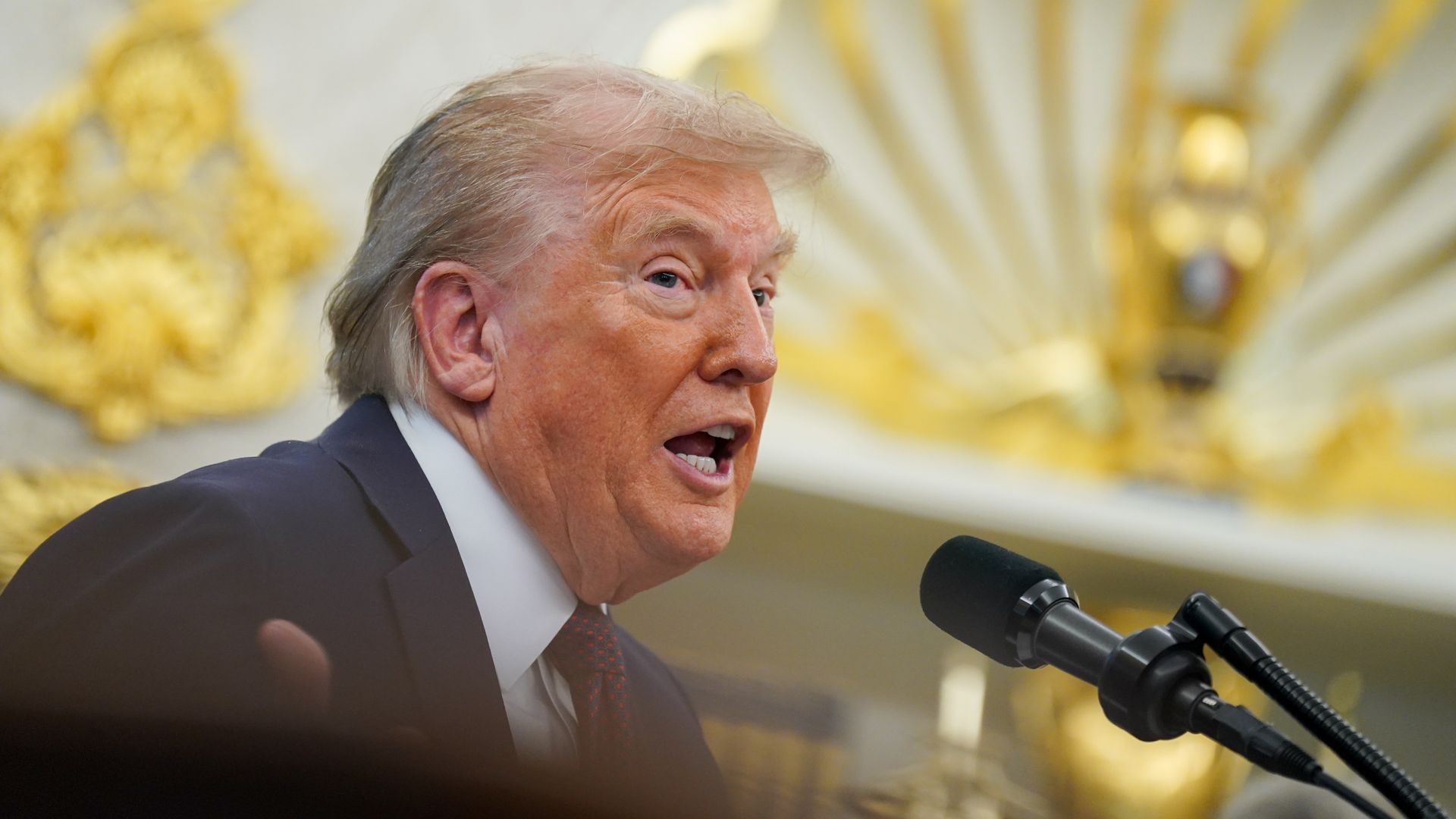 President Donald Trump with mouth open speaking into a microphone.