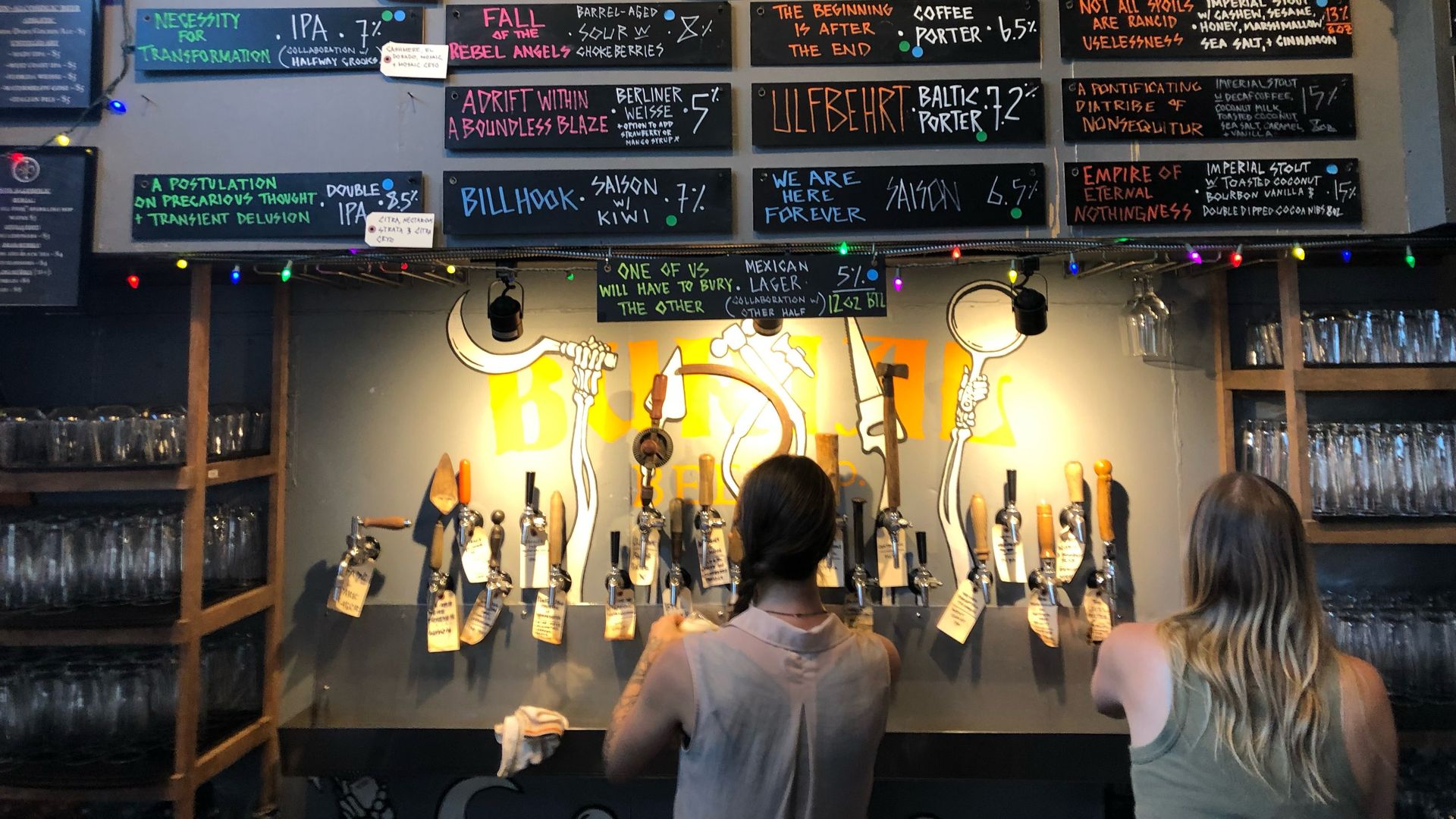 Barista pours a beer out of a beer tap. there are signs above her with all the beers on tap.