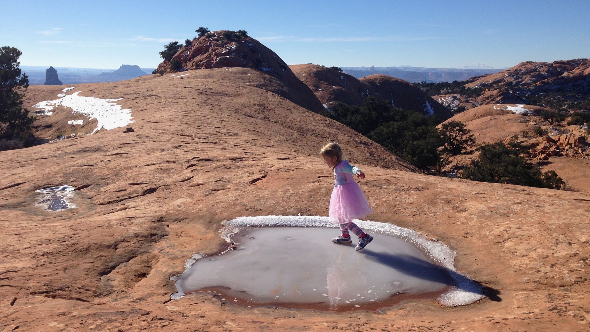 A little girl slides on a frozen puddle in the red rock desert.