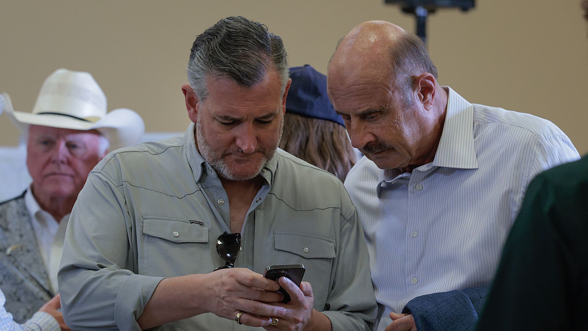 Sen. Ted Cruz (R-TX) and tv personality Dr. Phil McGraw look down at a cell phone and talk before participating in a roundtable event.