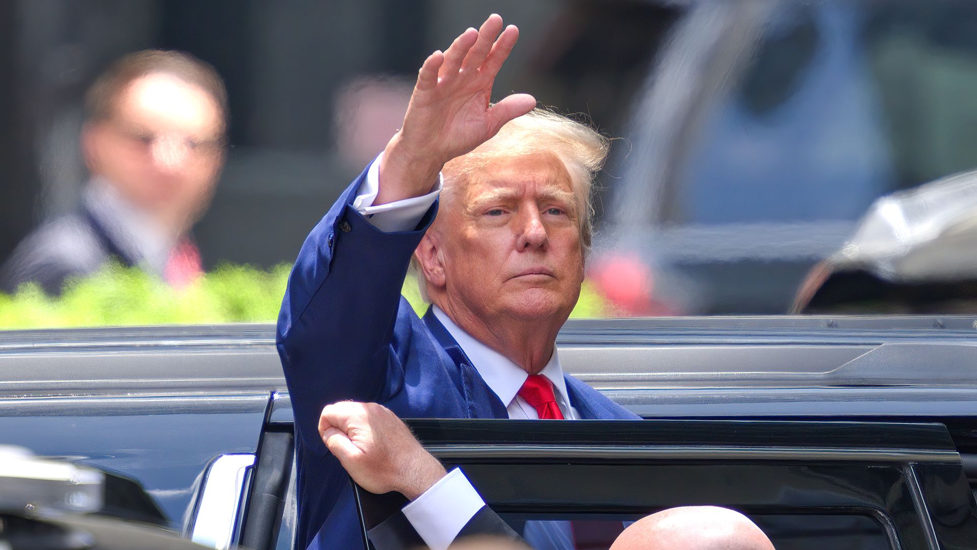 Former President Trump, lifting his hand as he steps into a car.