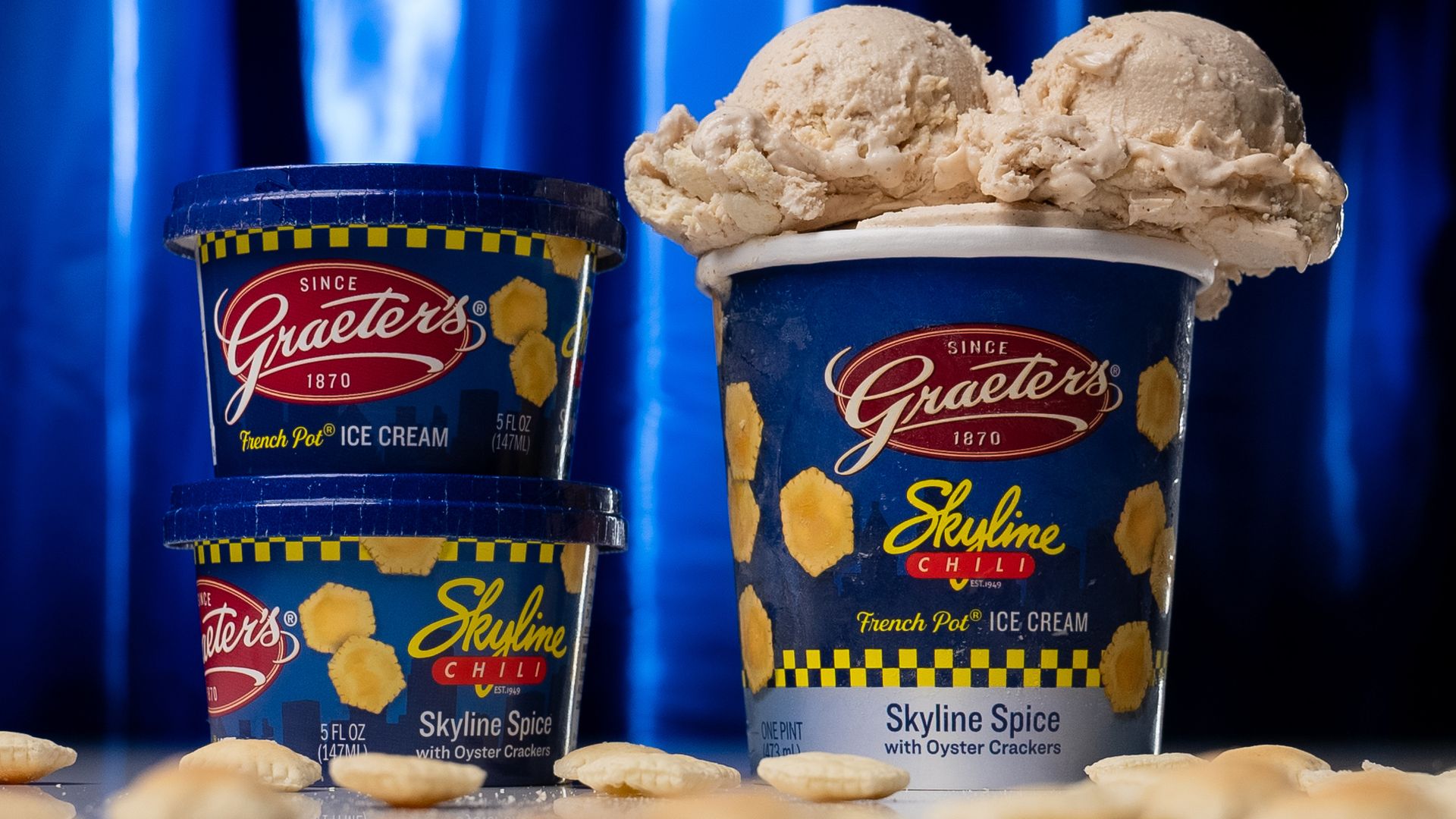 Graeter's ice cream containers that say Skyline Chili French Pot Ice Cream on them. The container to the right, which is a pint size, has two scoops of ice cream on top. There is also oyster crackers around the containers