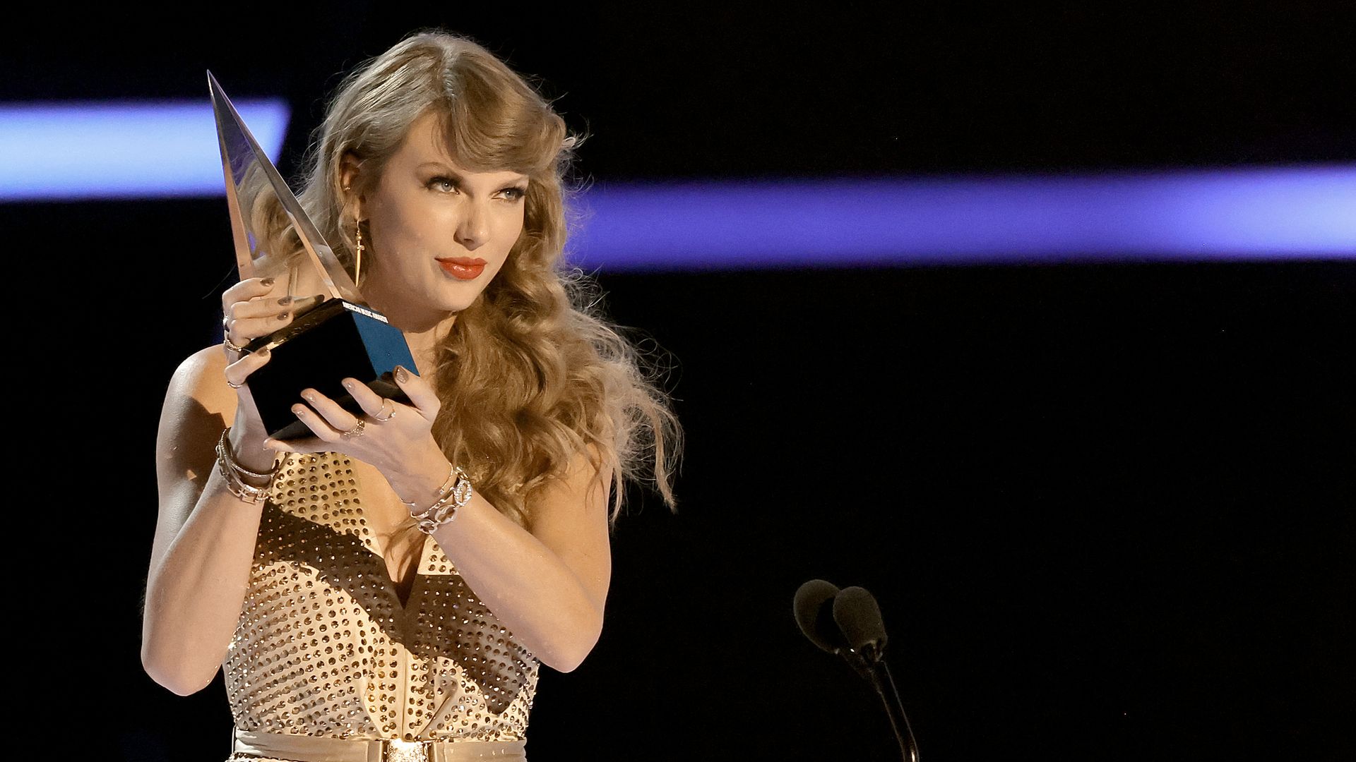 A woman with honey blonde hair holds a triangular shaped trophy in her hands while looking off camera.