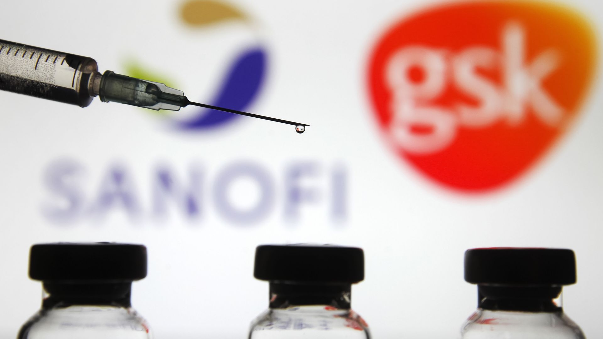 Sanofi and GSK signs in front of a syringe and vials.