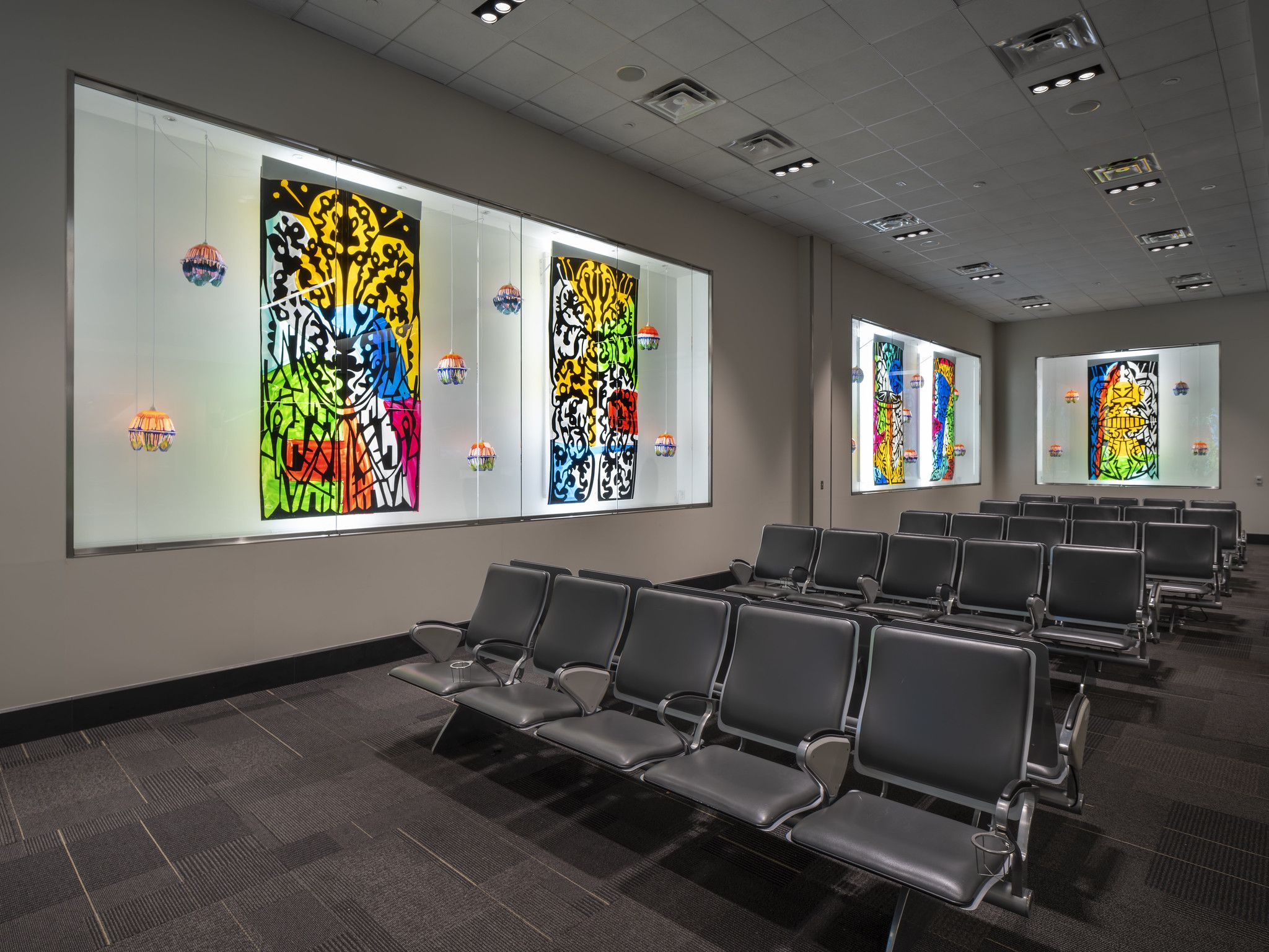 Colorful artworks and hanging lamps in light boxes at the gate of an airport. 