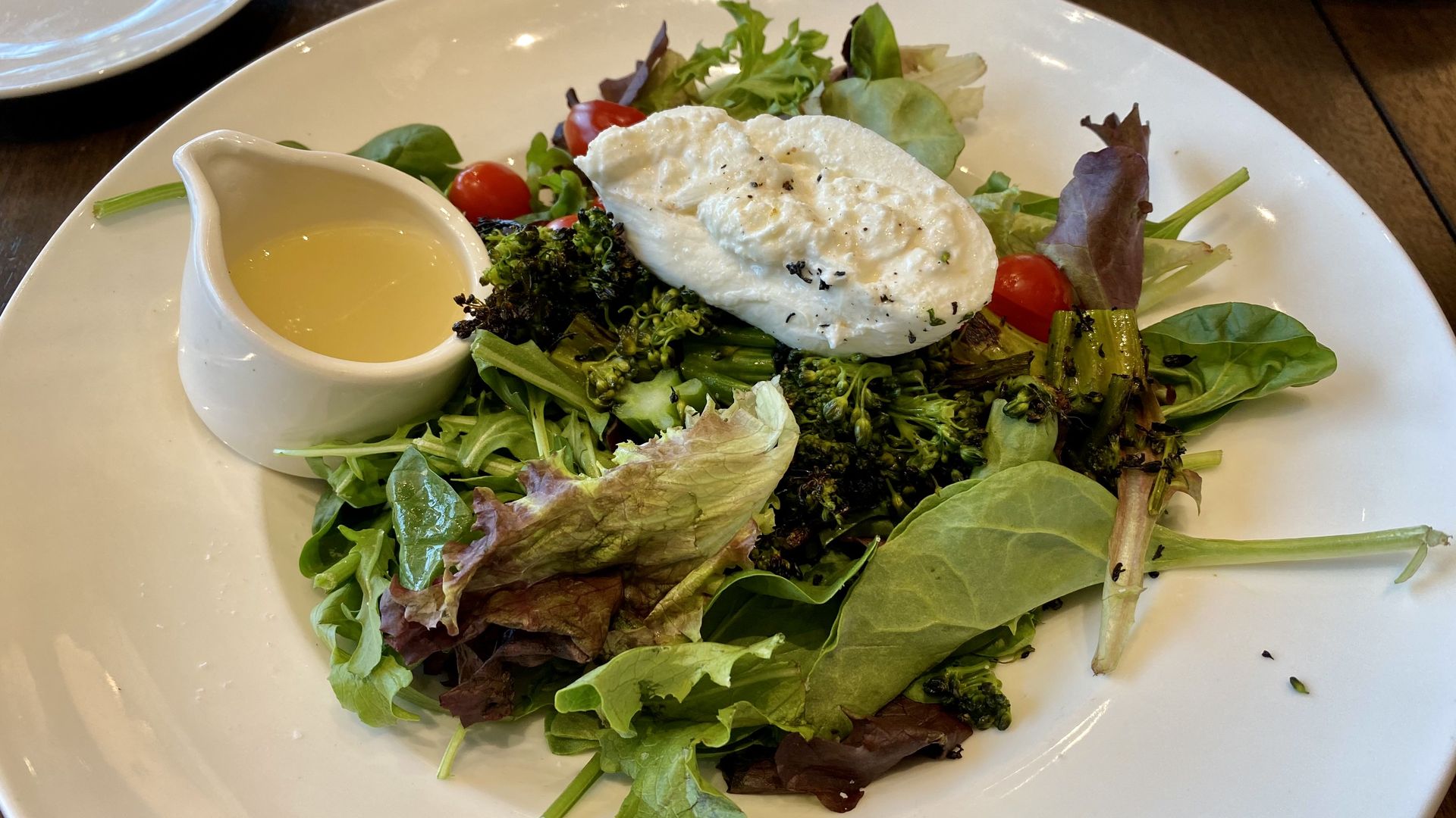 a salad with burrata on top and vinaigrette on the side