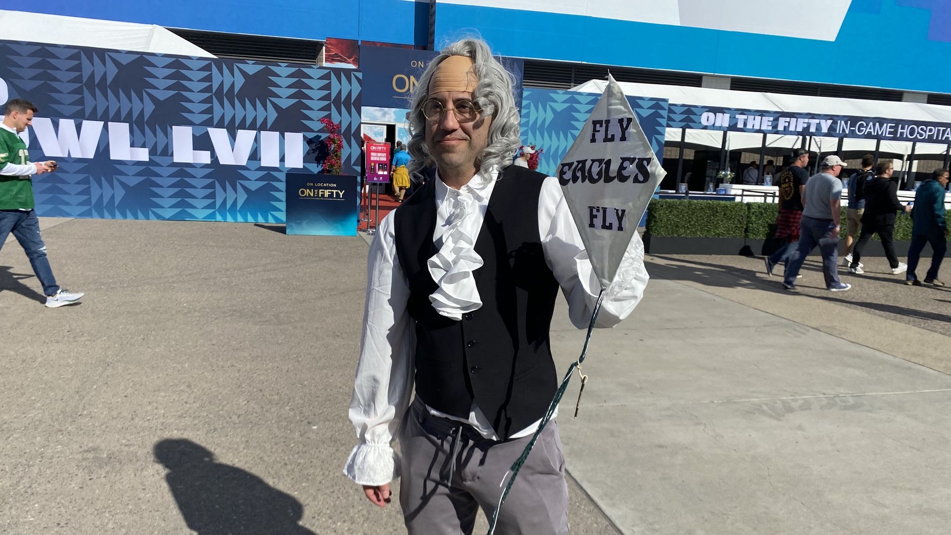 A man dressed as Benjamin Franklin holding a sign that says Fly Eagles Fly.