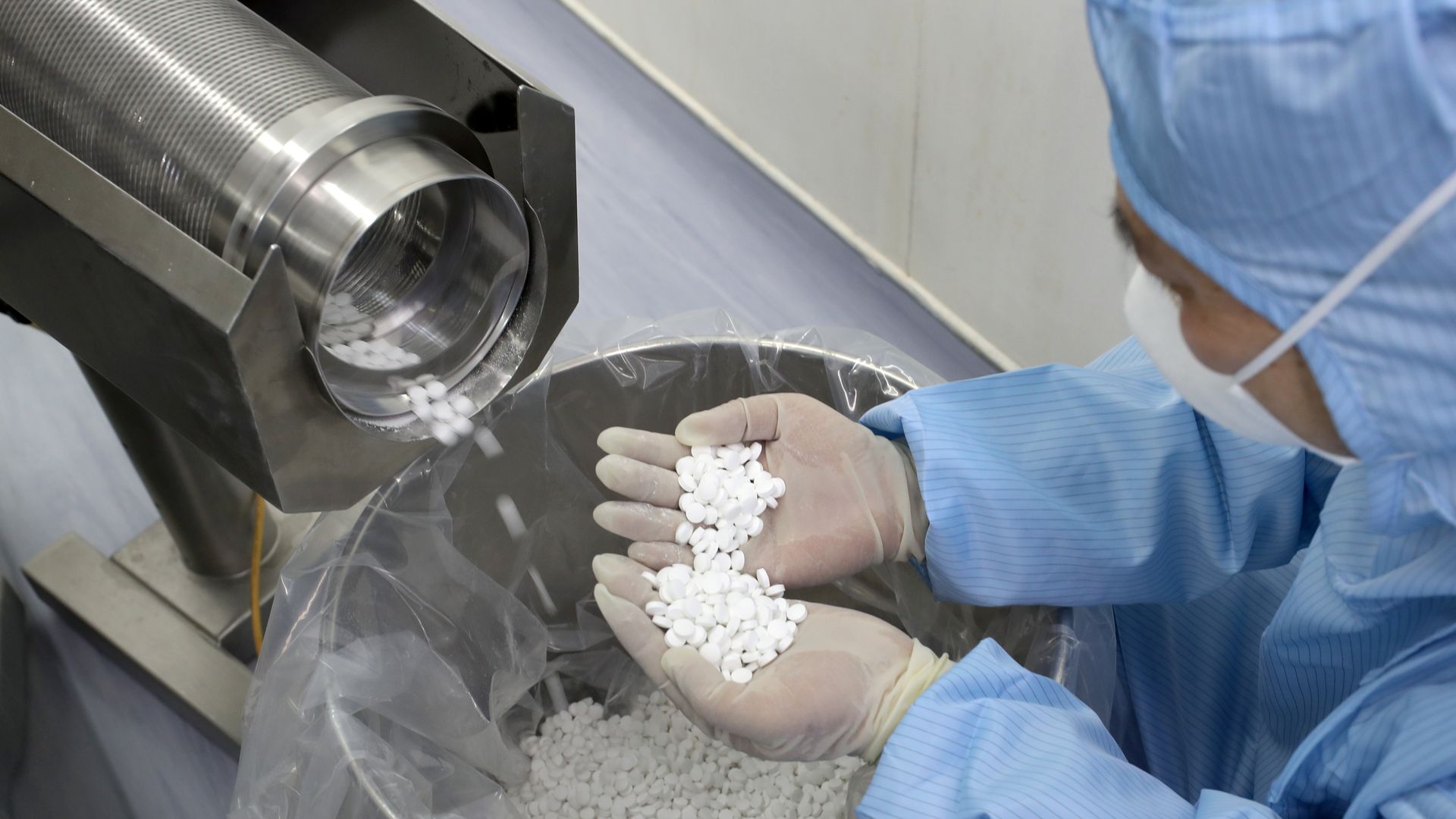 A worker in a blue gown and white mask inspects chloroquine tablets.