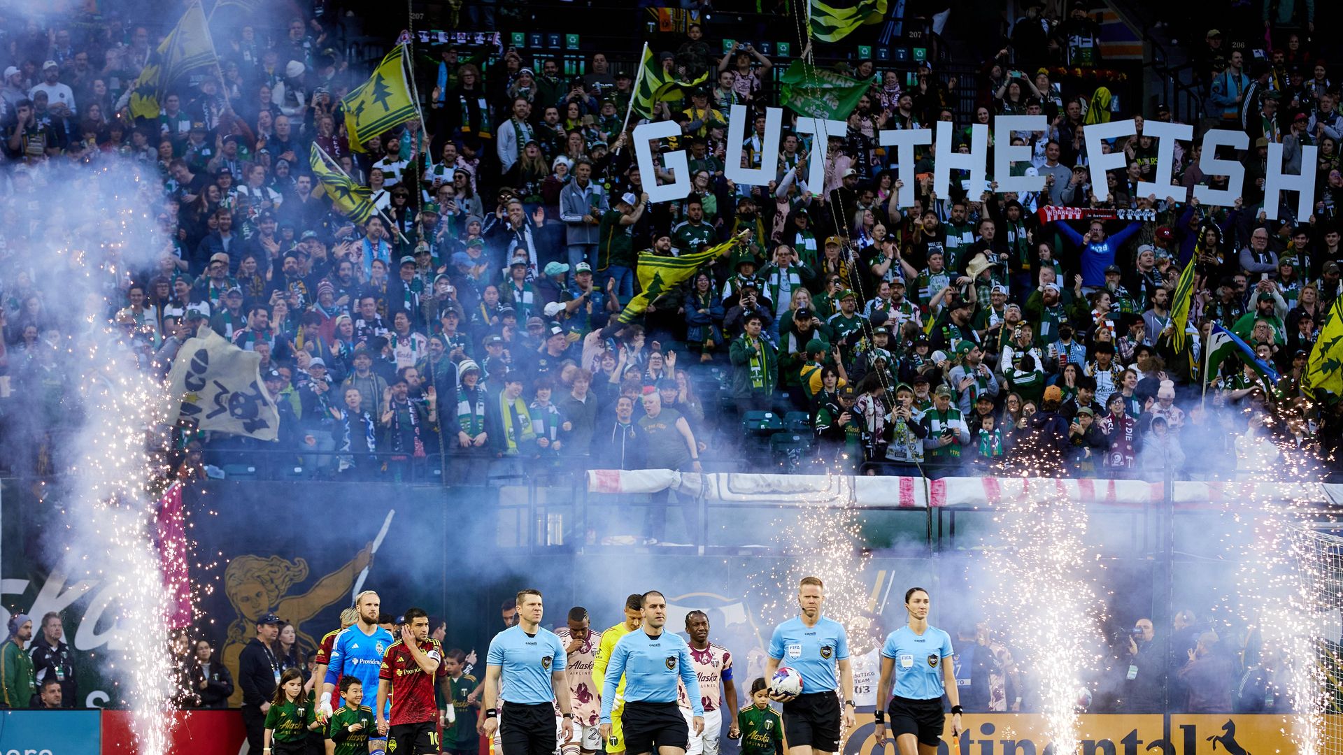 Soccer players take the field. in front of a banner saying GUT THE FISH