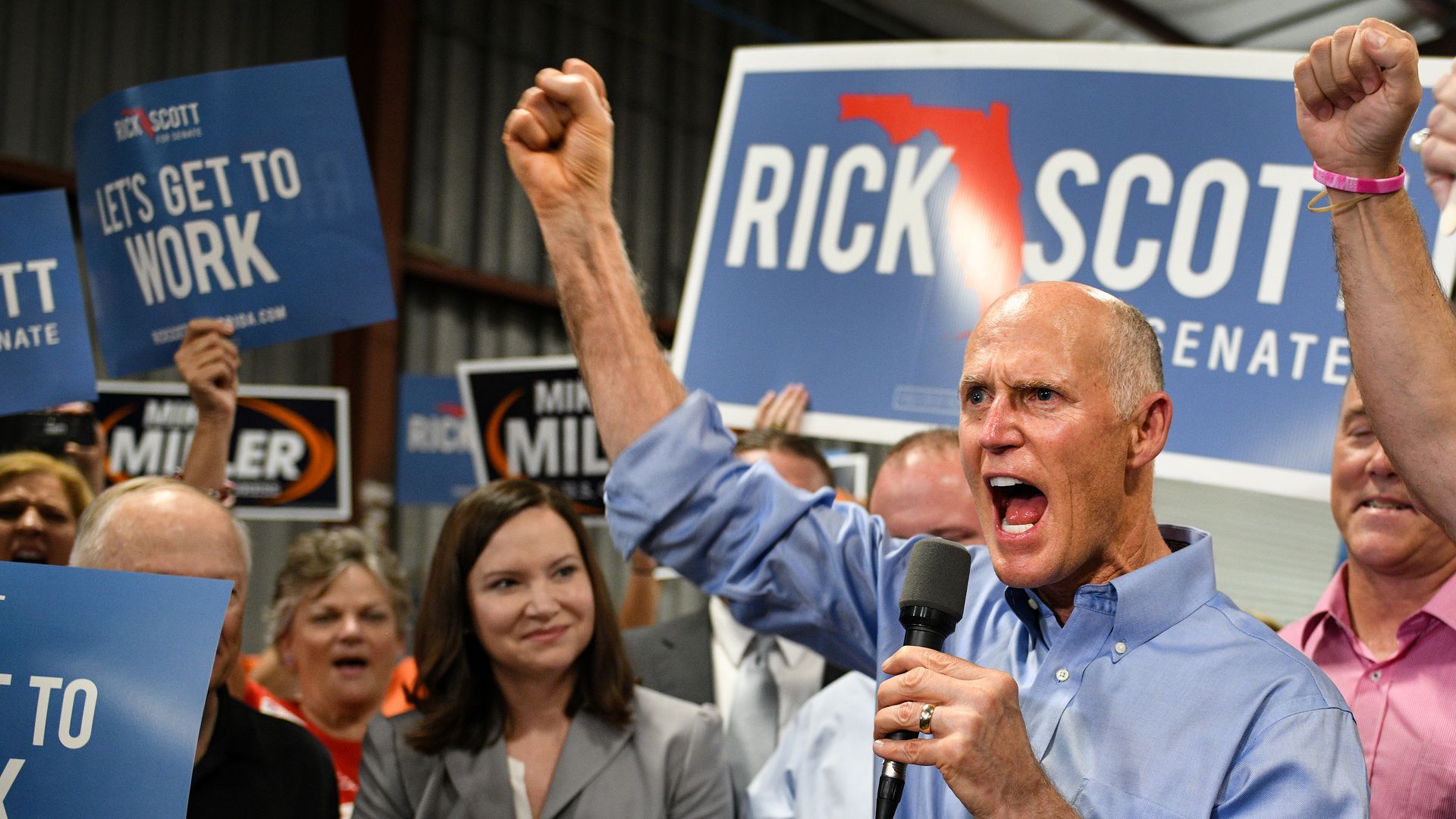Rick Scott exuberantly throws up his fist at a rally