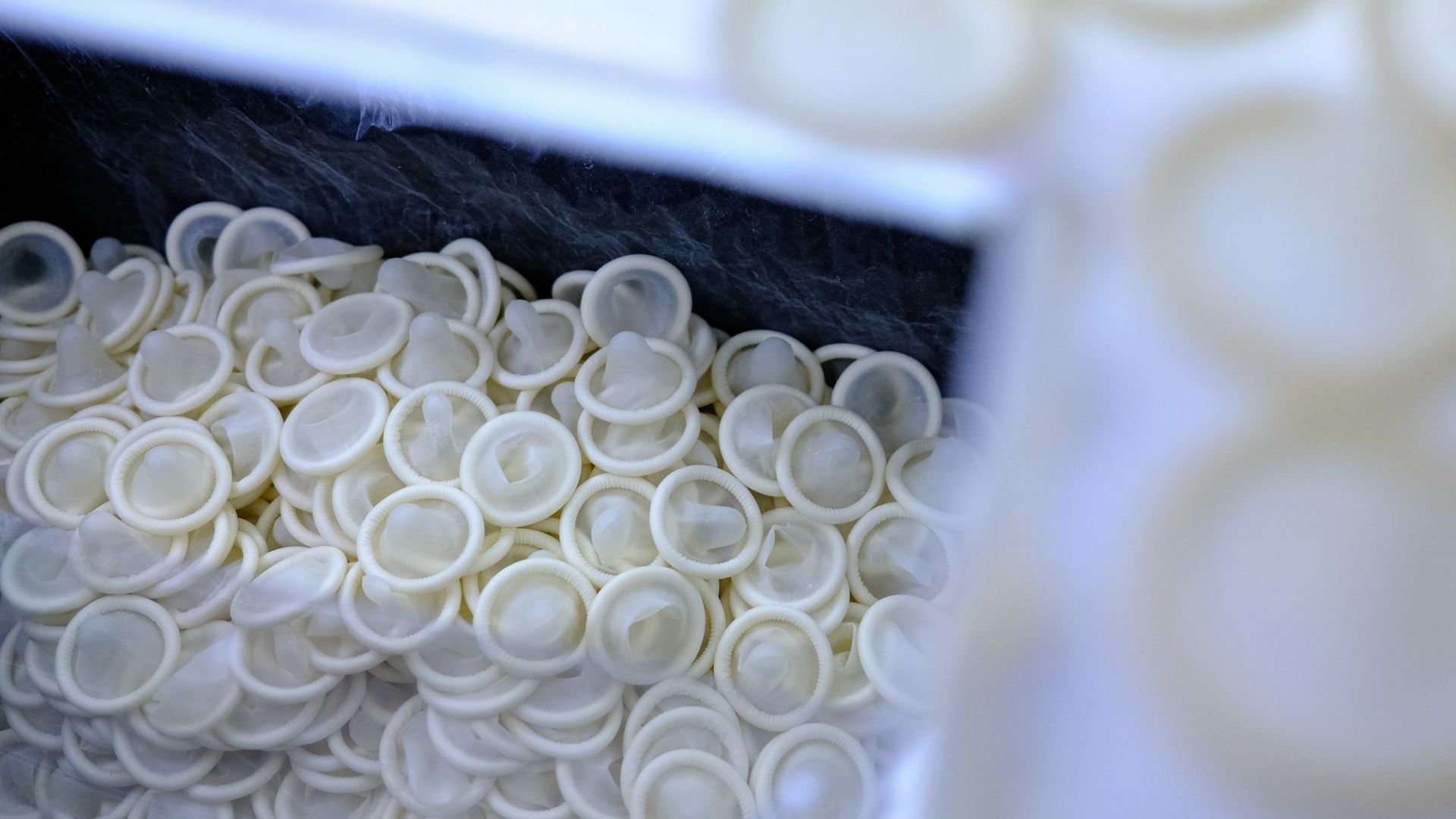 Close-up of a large pile of small white condoms; background is blurred white and blue.