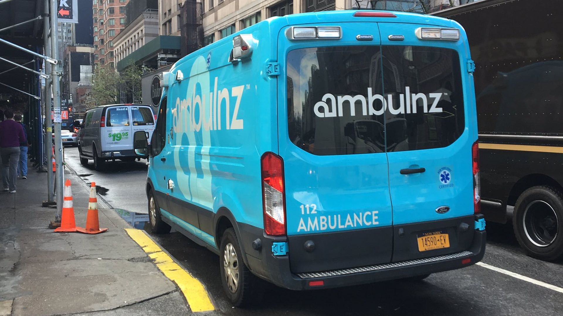 A blue Ambulnz patient transport truck on a street.