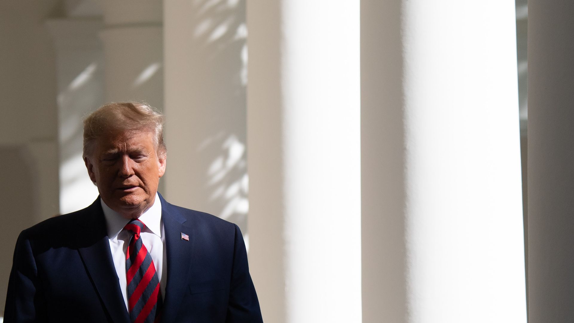 In this image, Trump walks past some pillars.