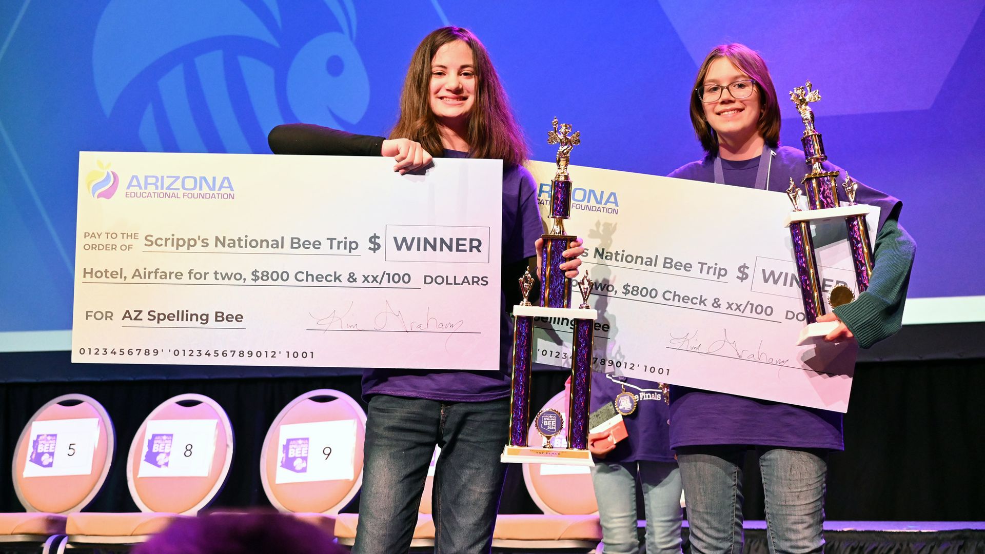 Two teenage girls post with trophies and oversized novelty checks. 